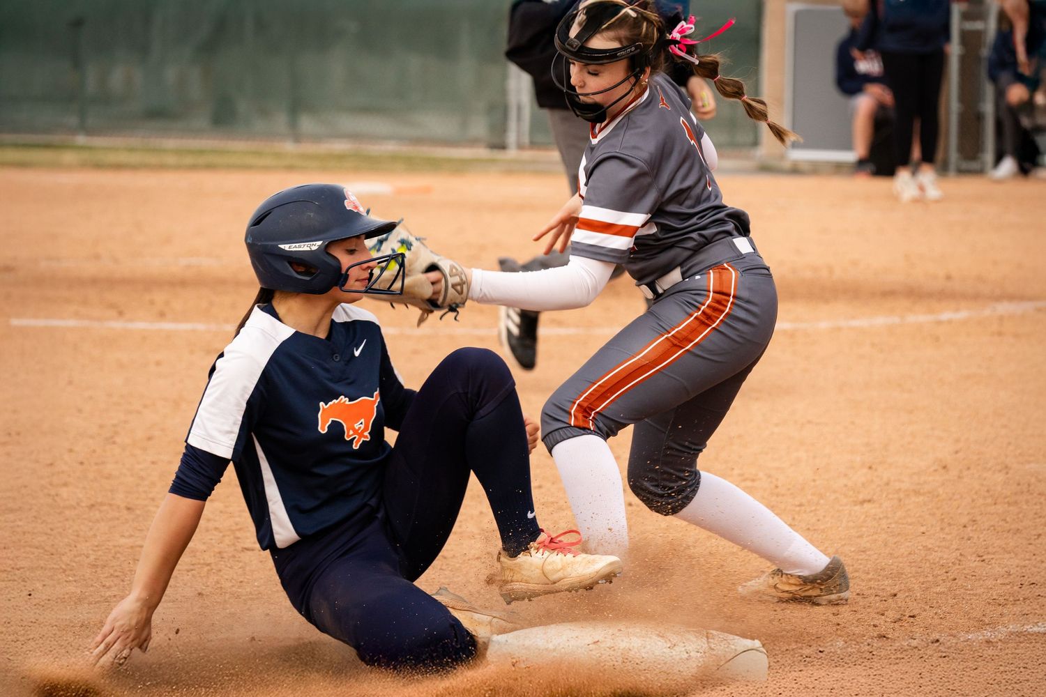Softball player slides into base as fielder attempts tag during competitive game.
