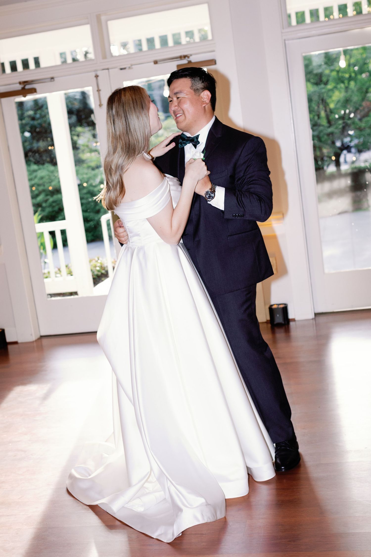Wedding couple performs dramatic dance dips on a hardwood ballroom floor with bright windows.