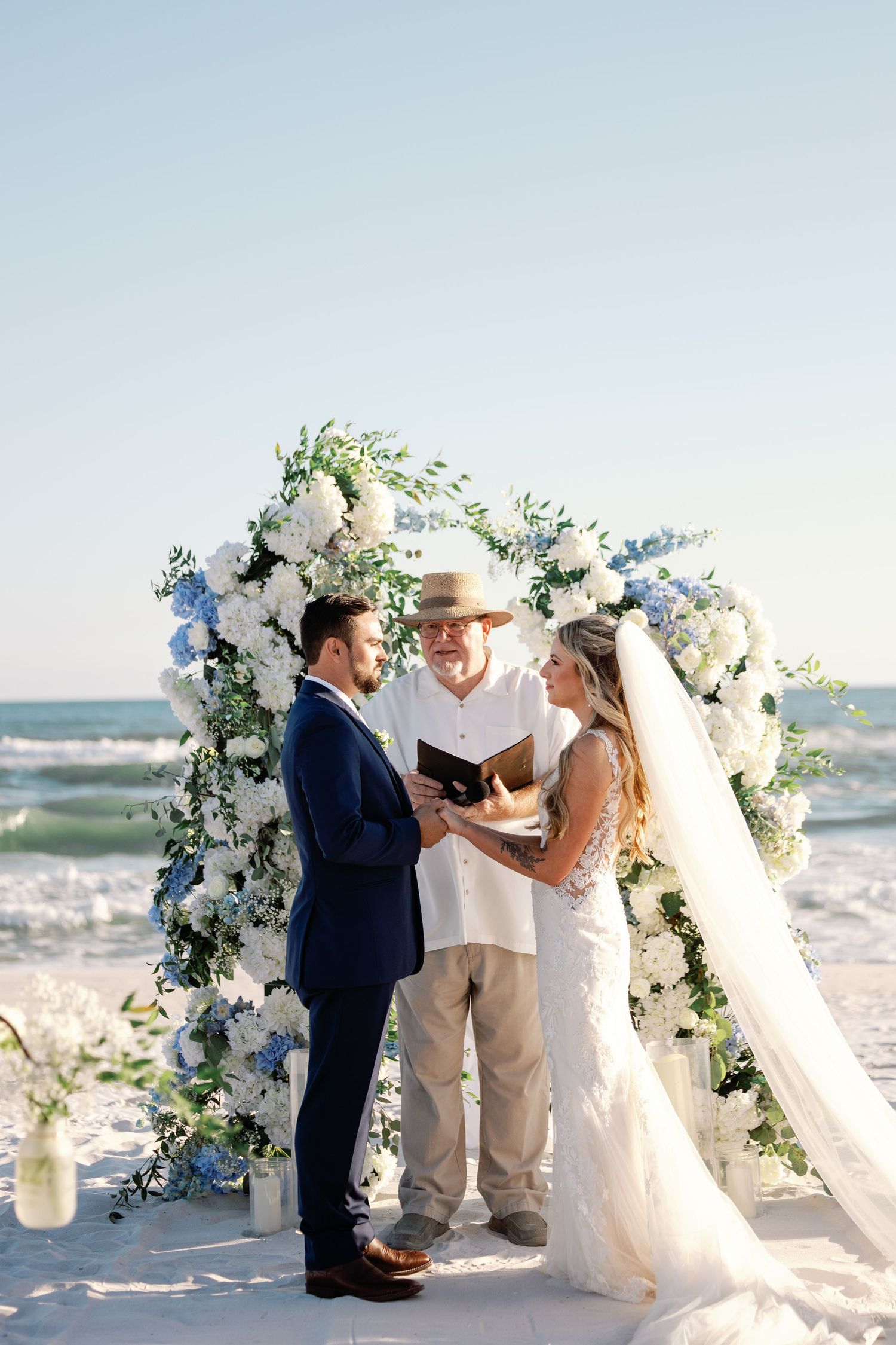 Beach wedding ceremony with floral arch decorated in white and blue flowers.