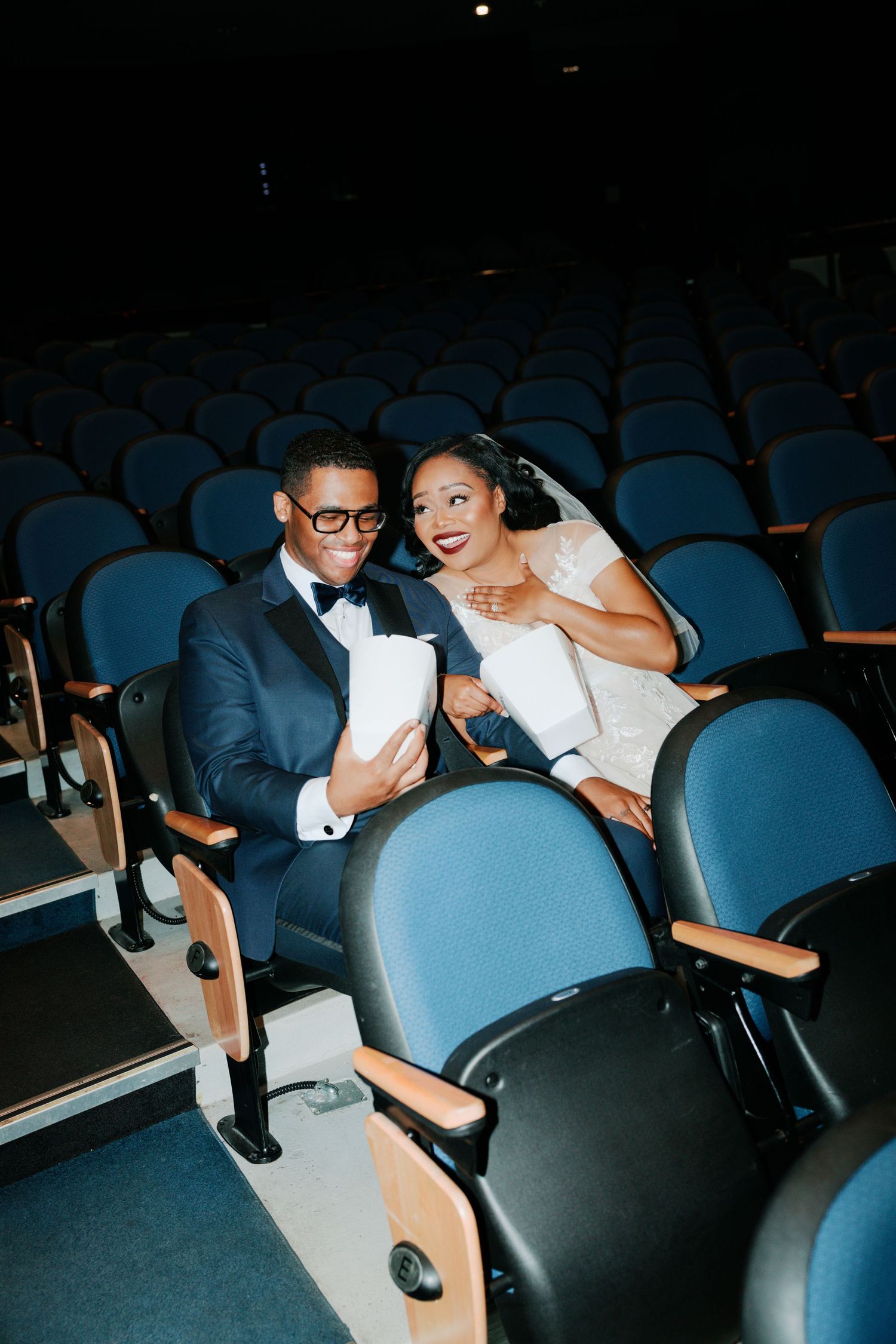 Newlyweds sharing laughter while seated in blue theater chairs.