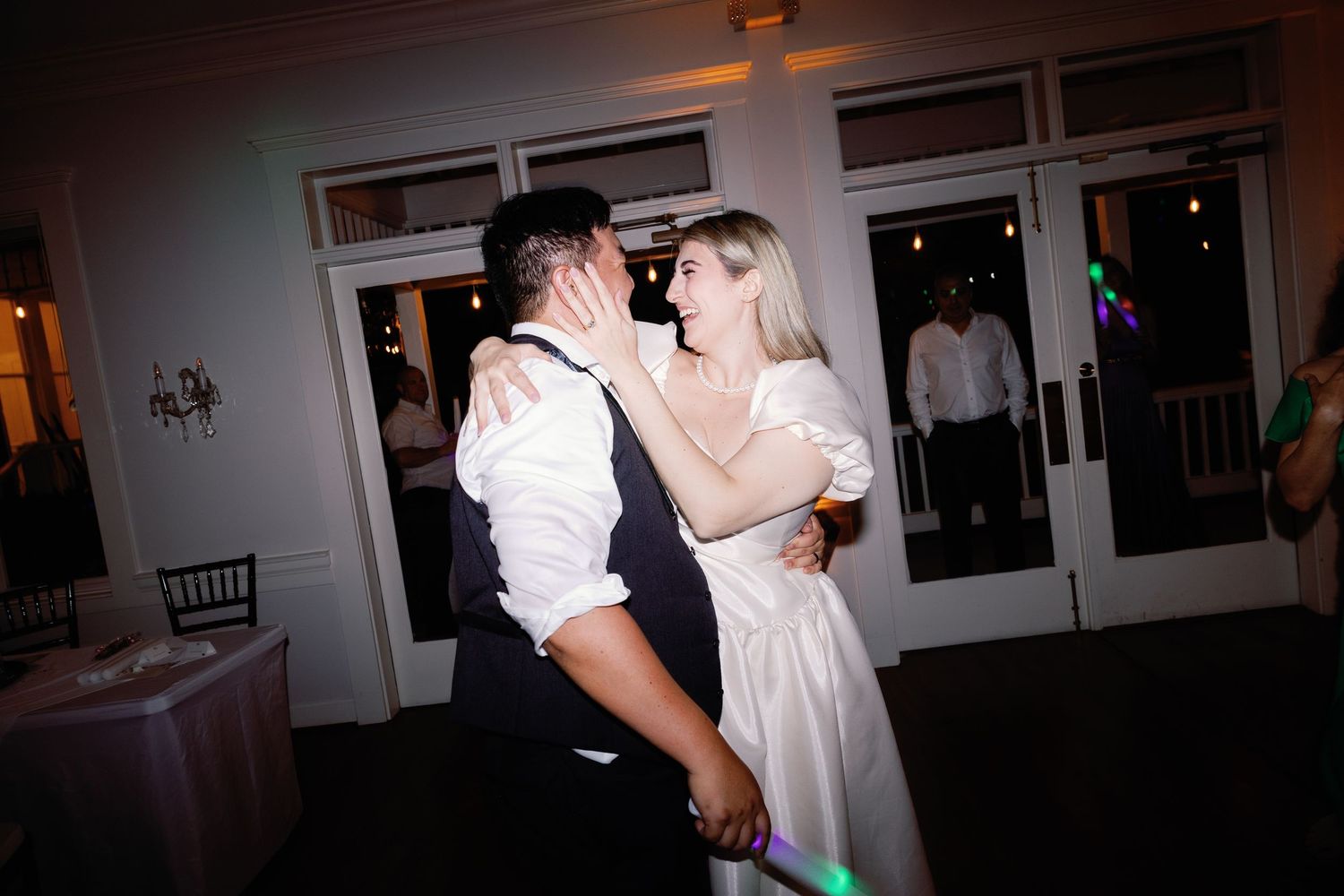 Wedding reception guests dance in a dimly lit room with soft ambient lighting.