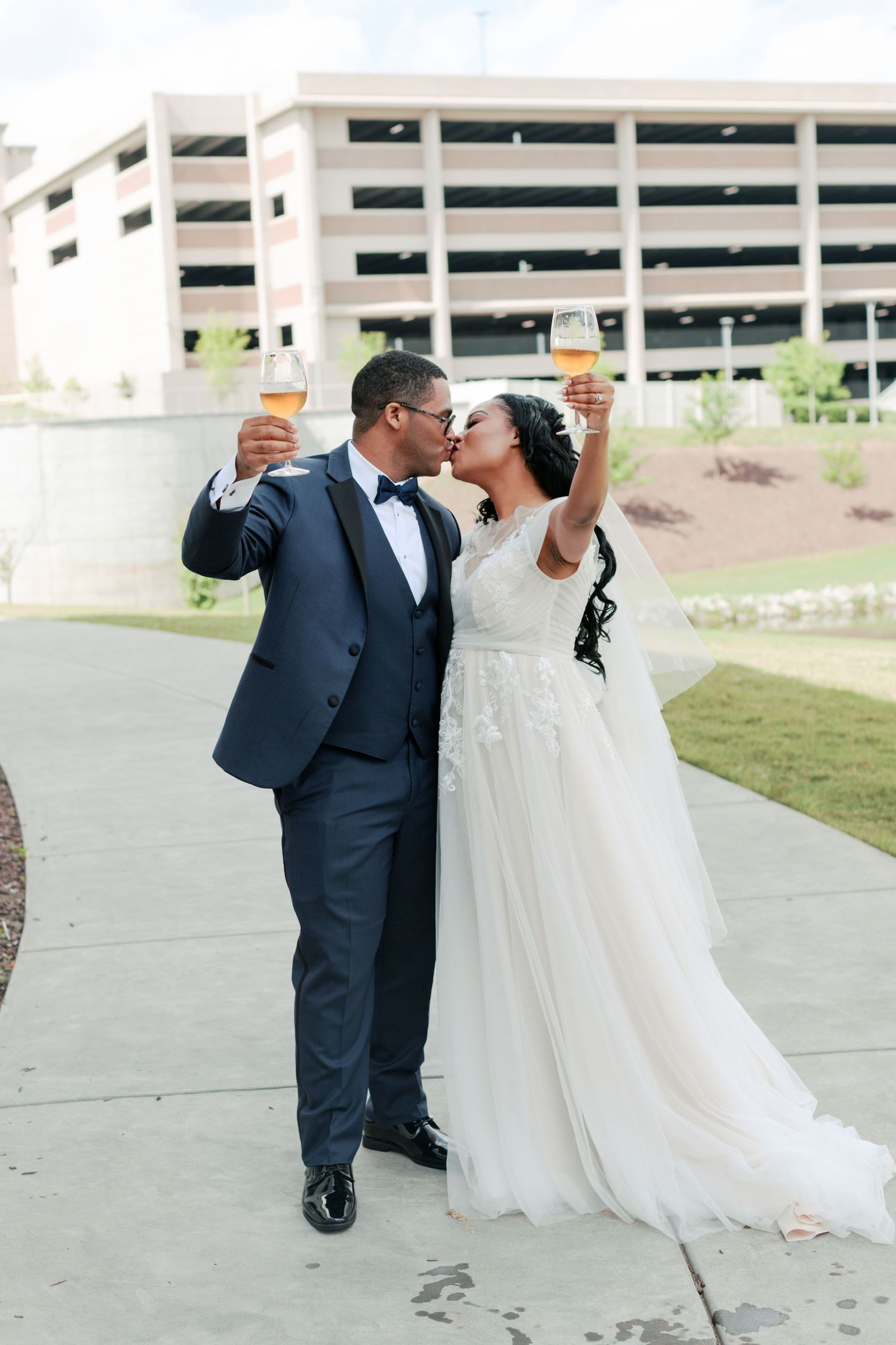 Newlyweds toasting and sharing a romantic moment outside a parking structure.