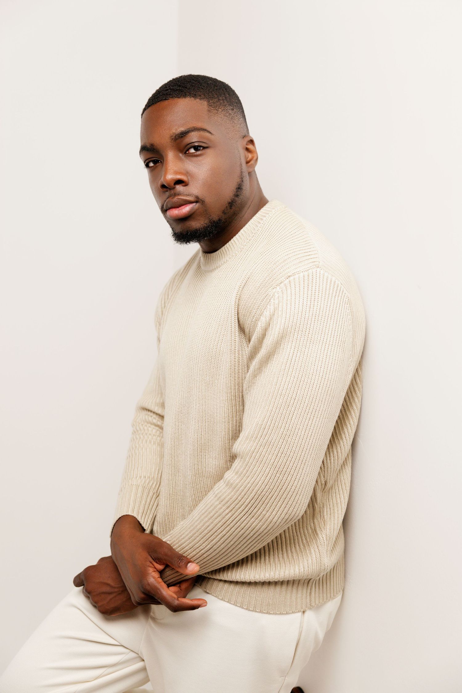 A professional photo of someone wearing a beige sweater against a minimal white setting.