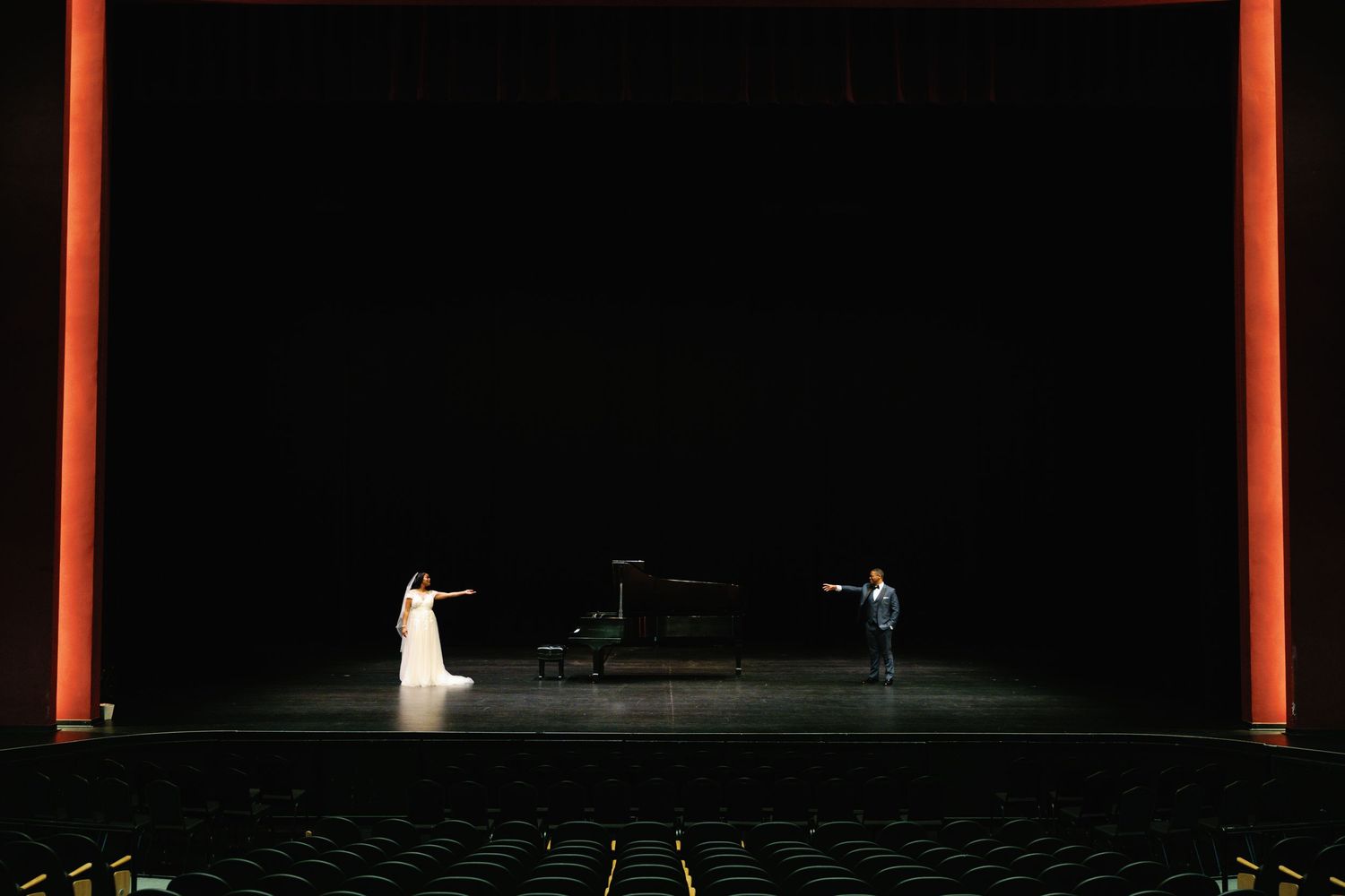 Dimly lit theater stage with red architectural lighting and minimal set pieces.