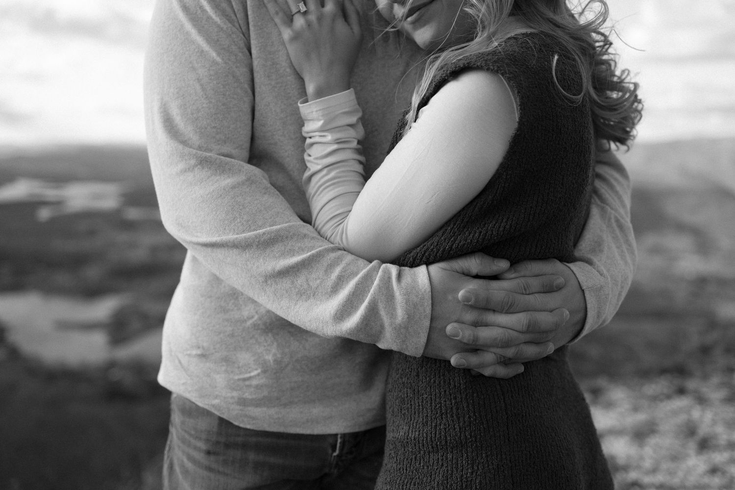 Couple sharing an intimate embrace on a mountain overlook with sweeping valley views.