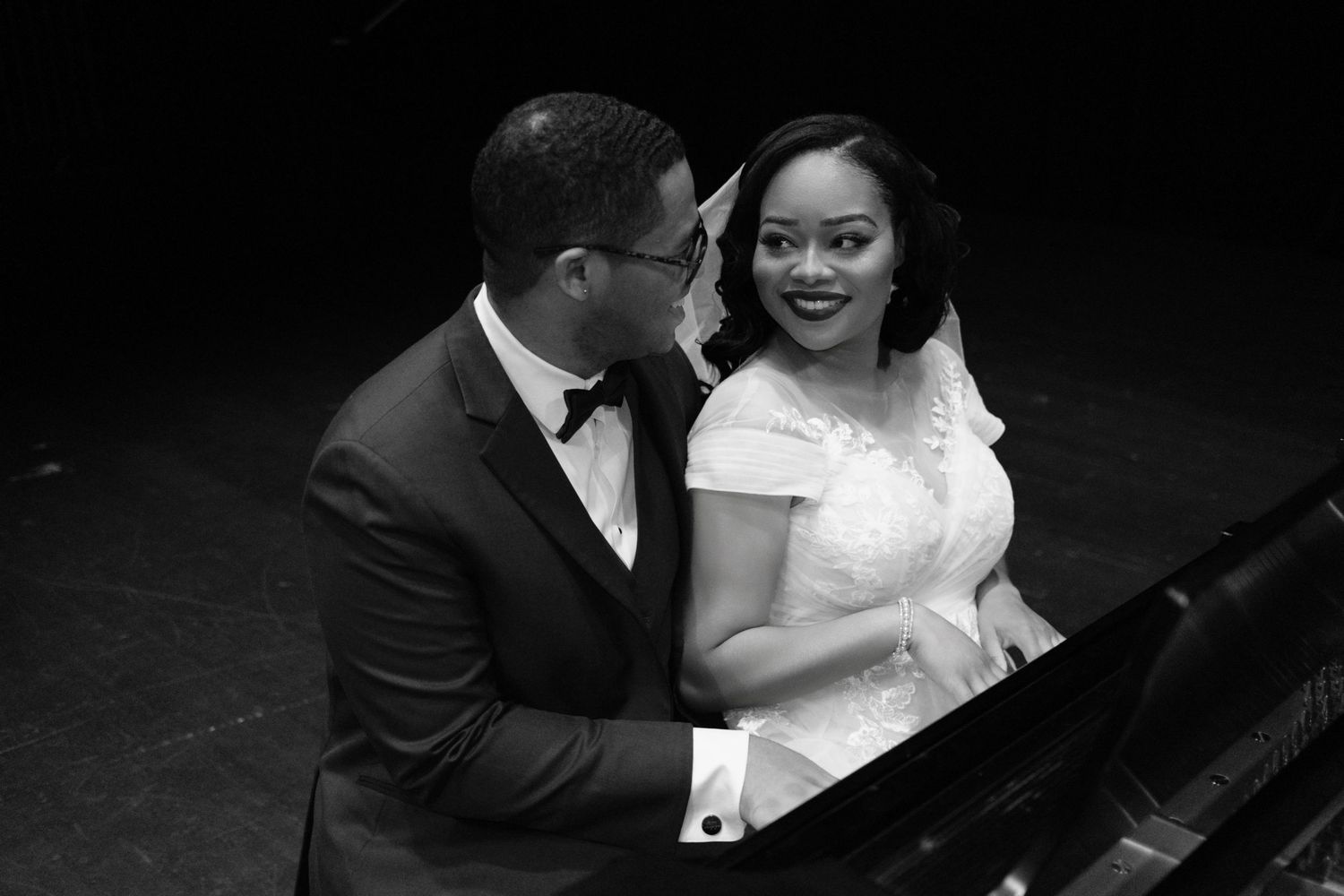 Romantic couple pose at piano in formal wedding attire.