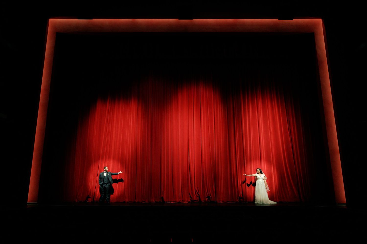 Theater stage with red curtain and dramatic lighting featuring performers in silhouette.