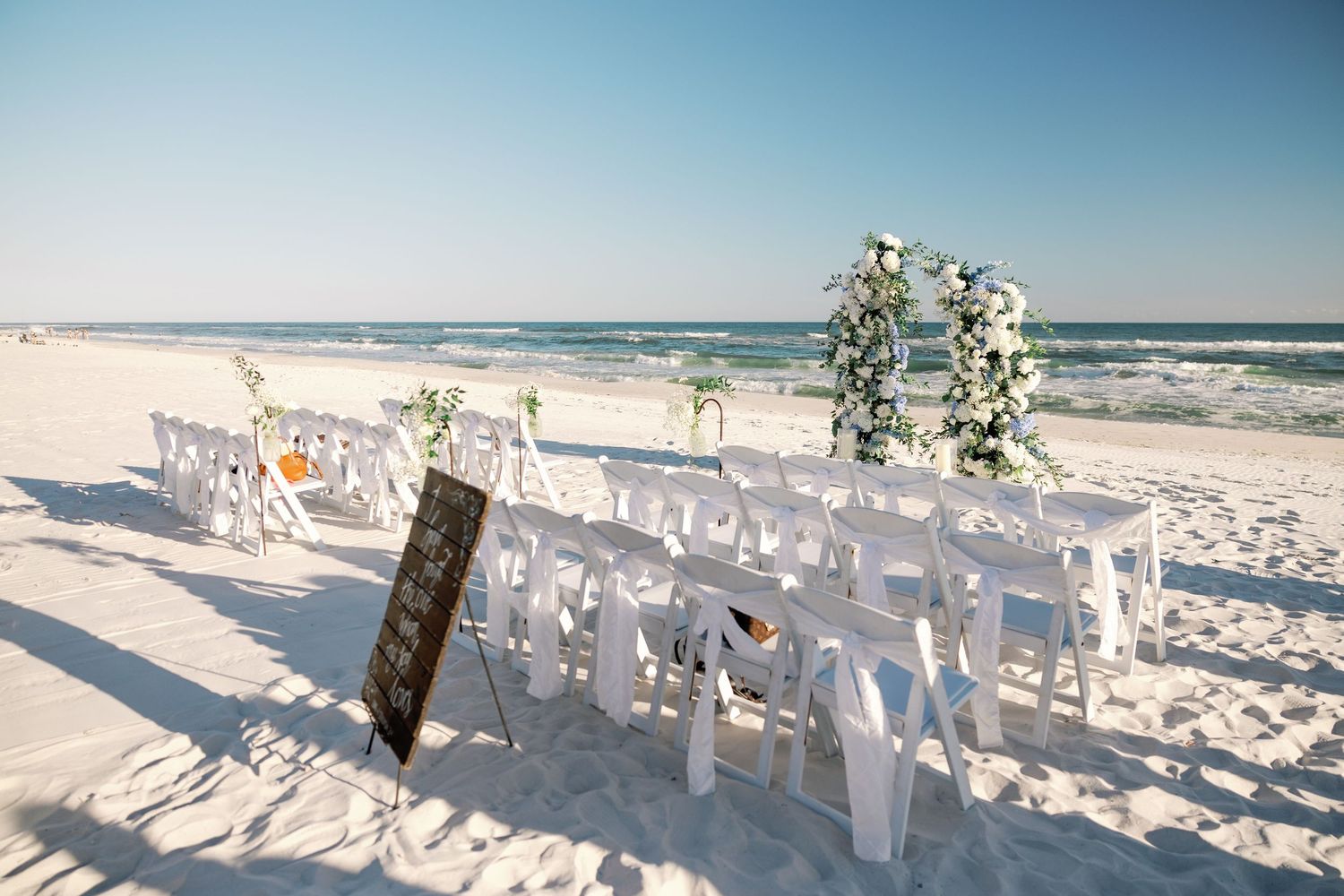Beach wedding ceremony setup with white chairs and reserved seating signs.