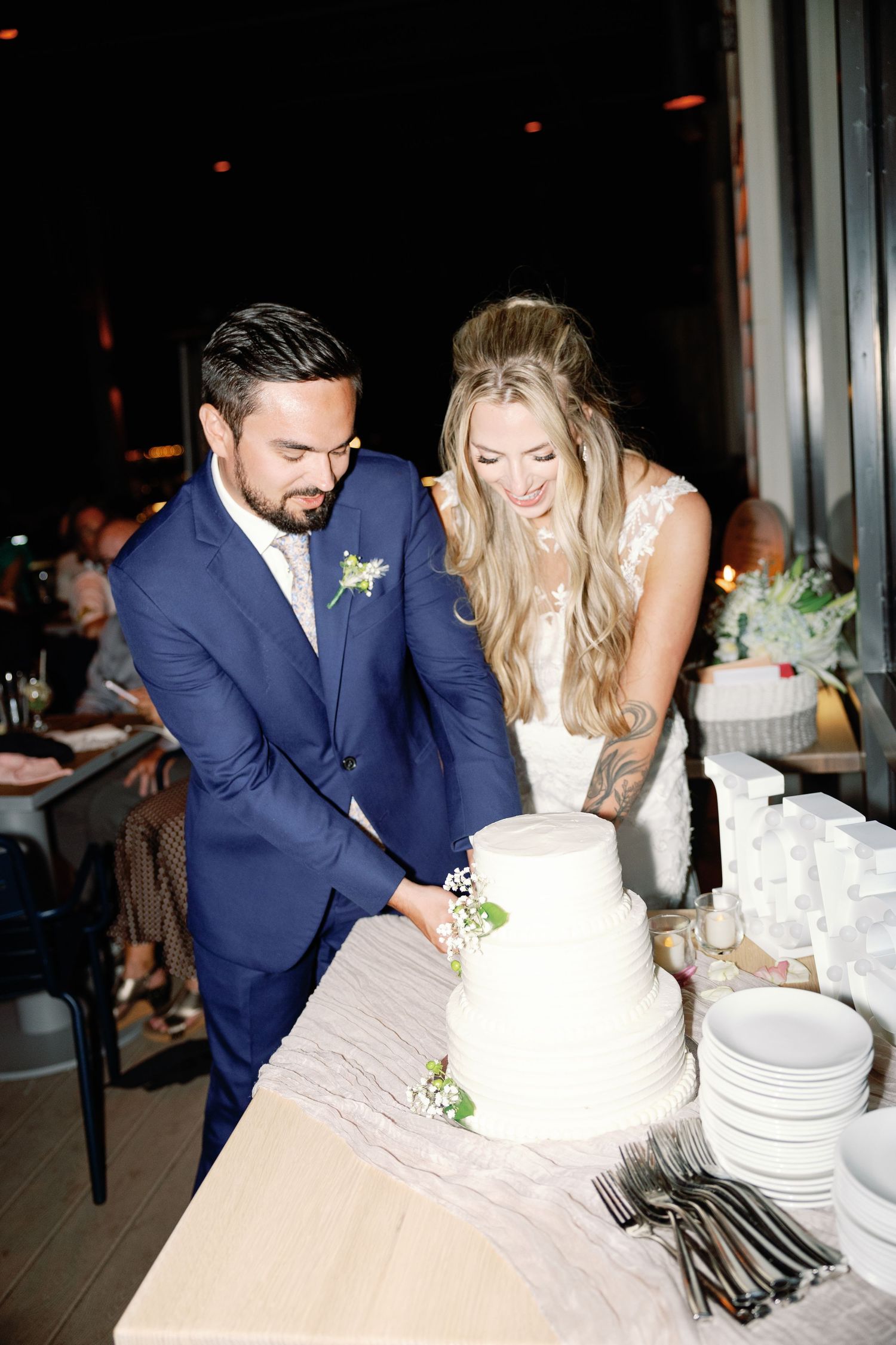 Couple cuts their white wedding cake together at evening reception.