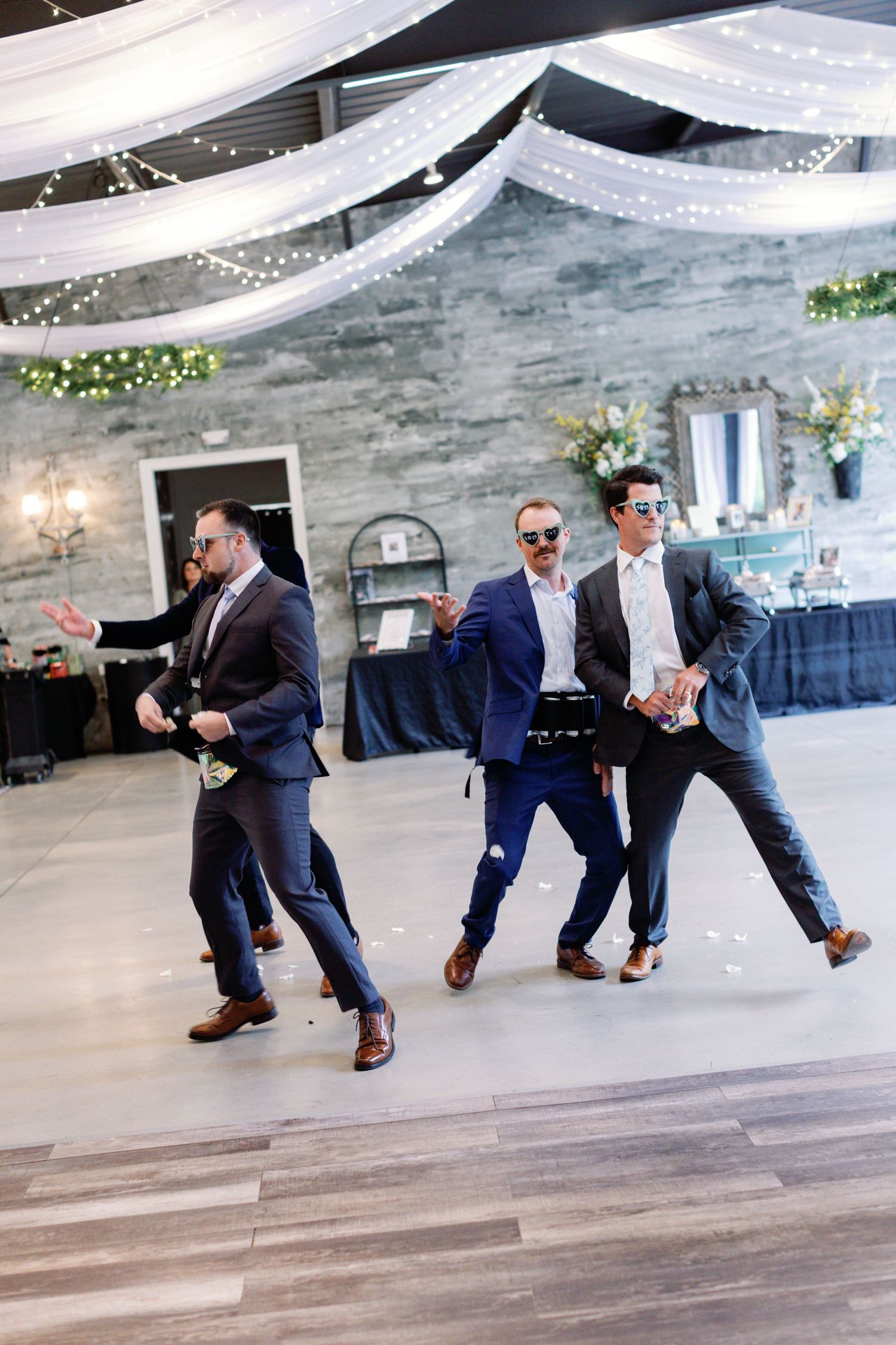 Series of groomsmen performing synchronized jump moves on indoor wooden floor.