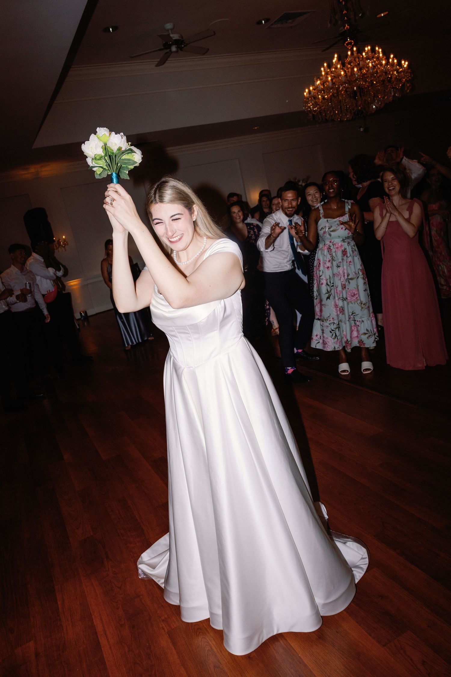 Bride twirls in her white wedding dress on the dance floor surrounded by guests.