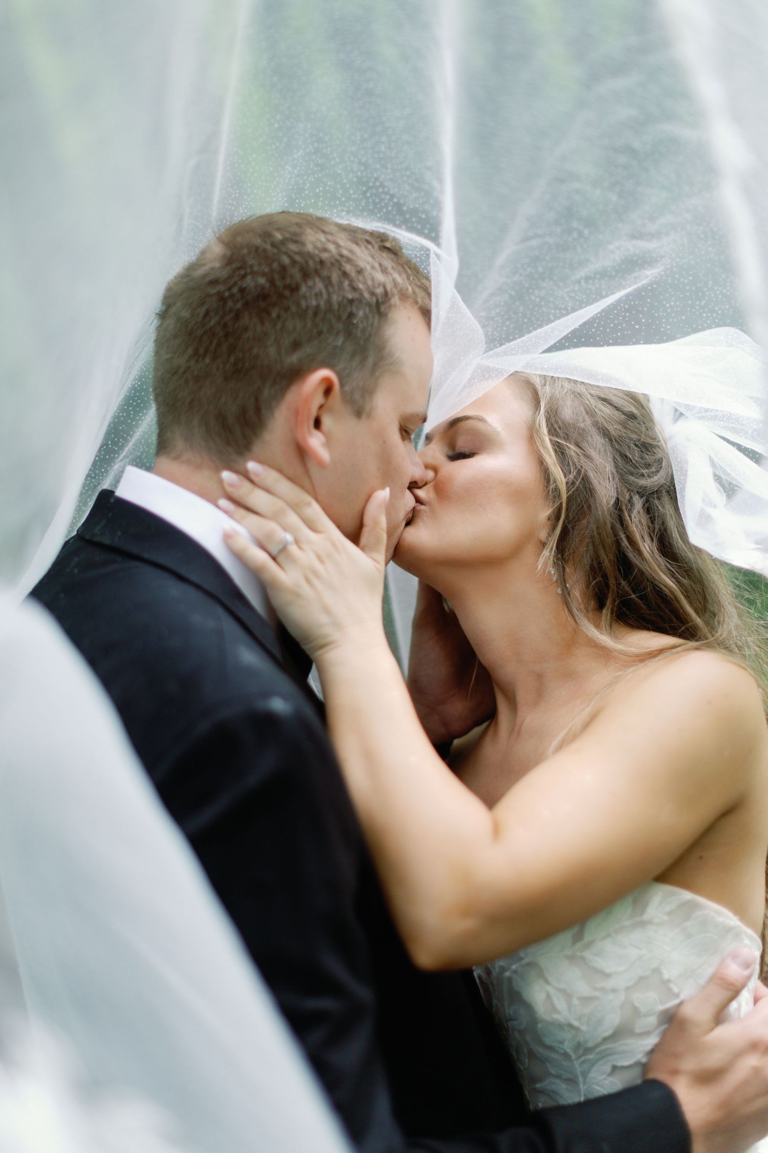 Romantic wedding couple sharing intimate kisses under a flowing white veil.