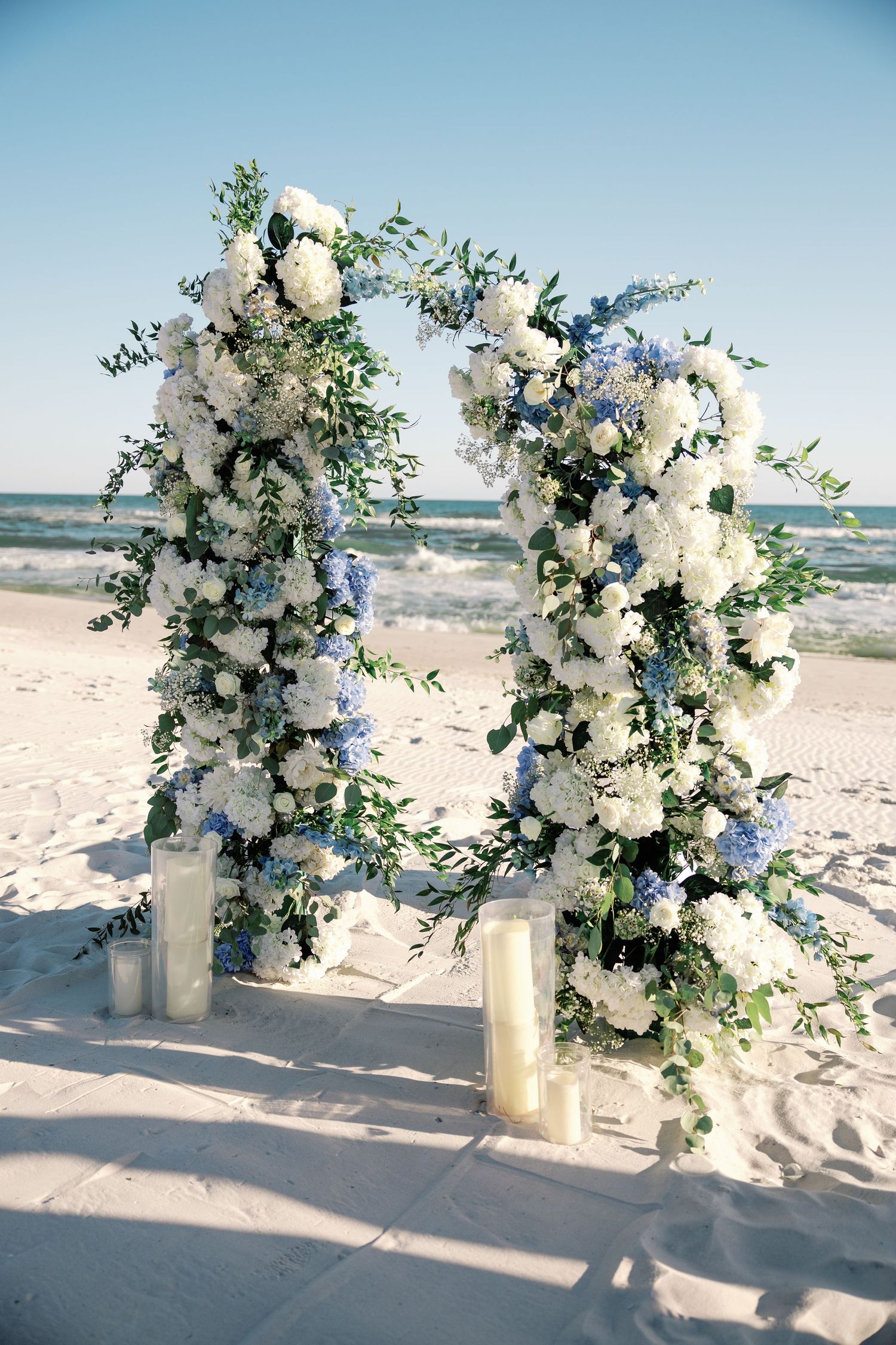 White and blue floral arrangements decorating beach wedding ceremony setup.