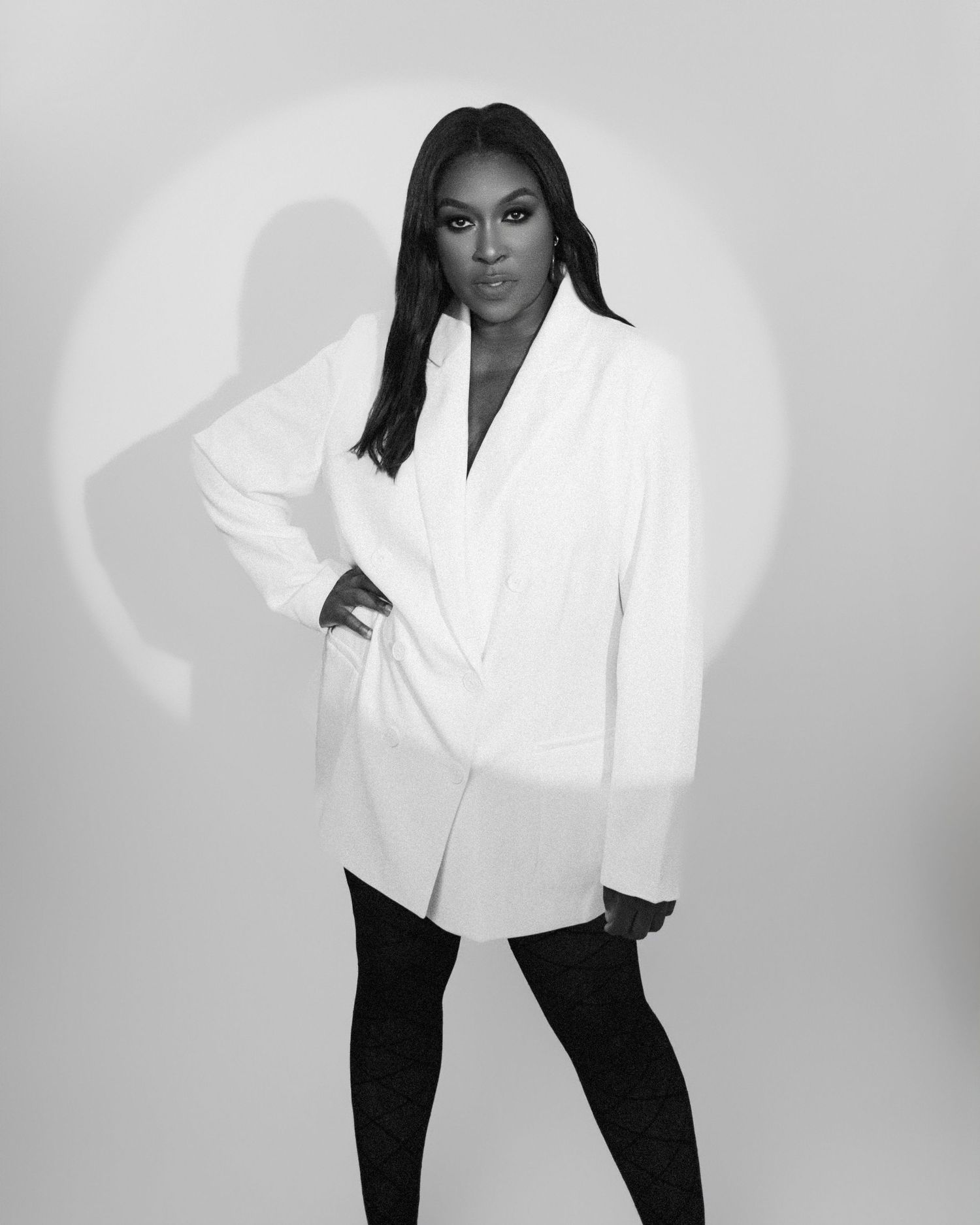 Fashion model in white blazer poses against grey studio background.
