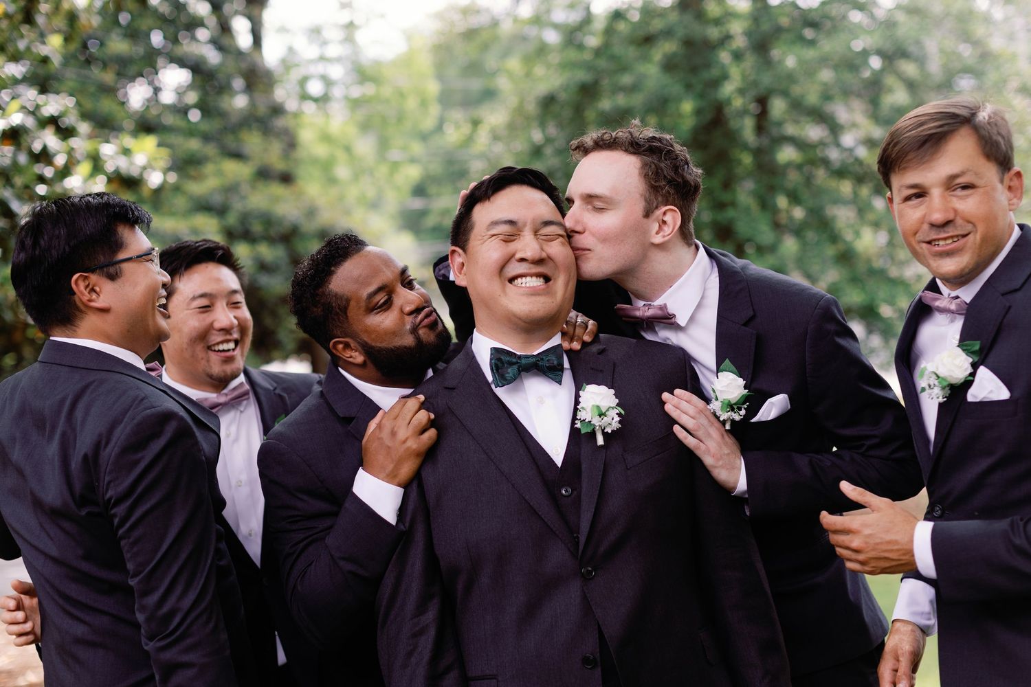 A candid moment captures the groomsmen sharing laughter during outdoor wedding photos.