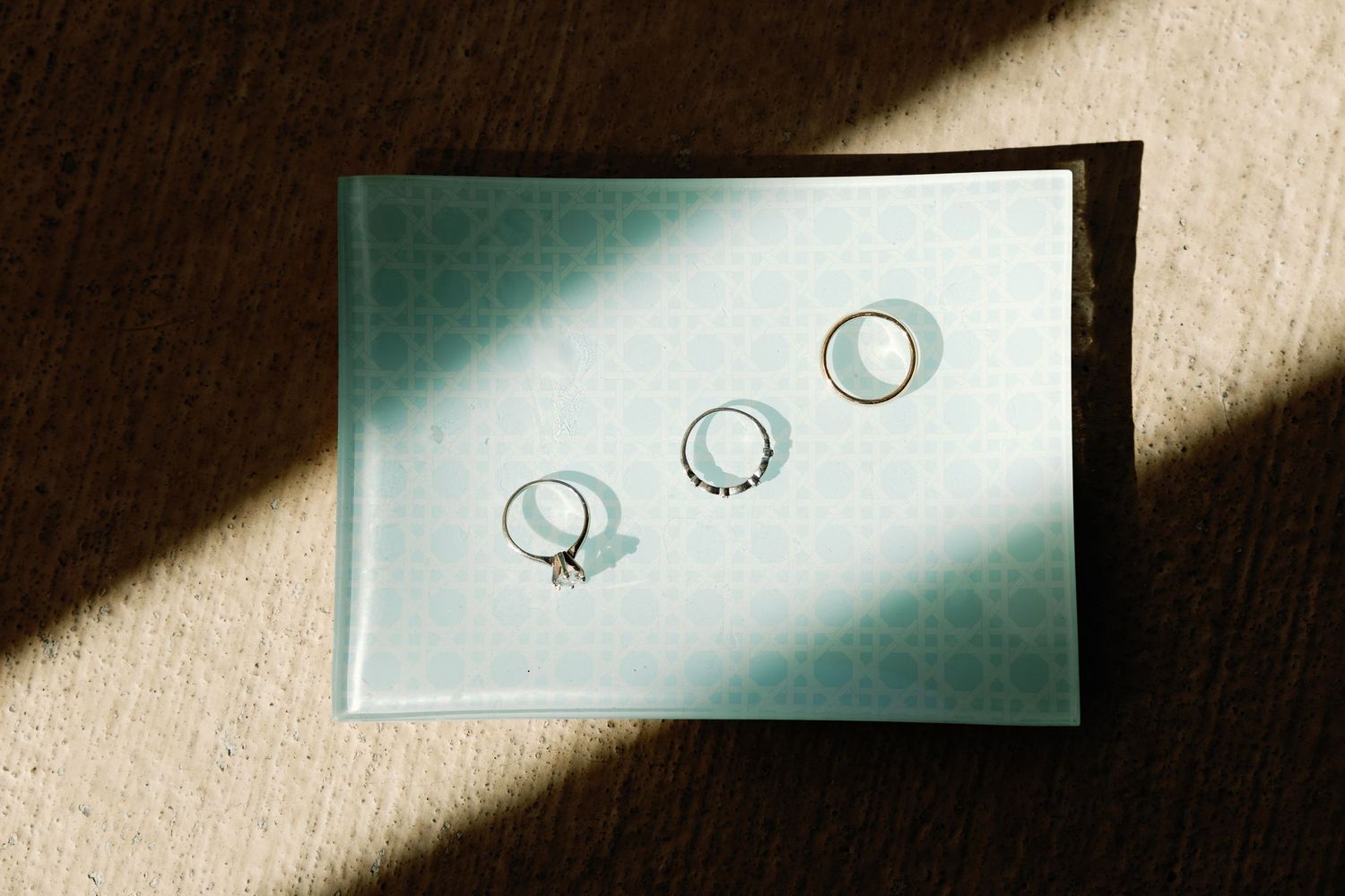 Wedding rings casting shadows on light blue invitation cards.