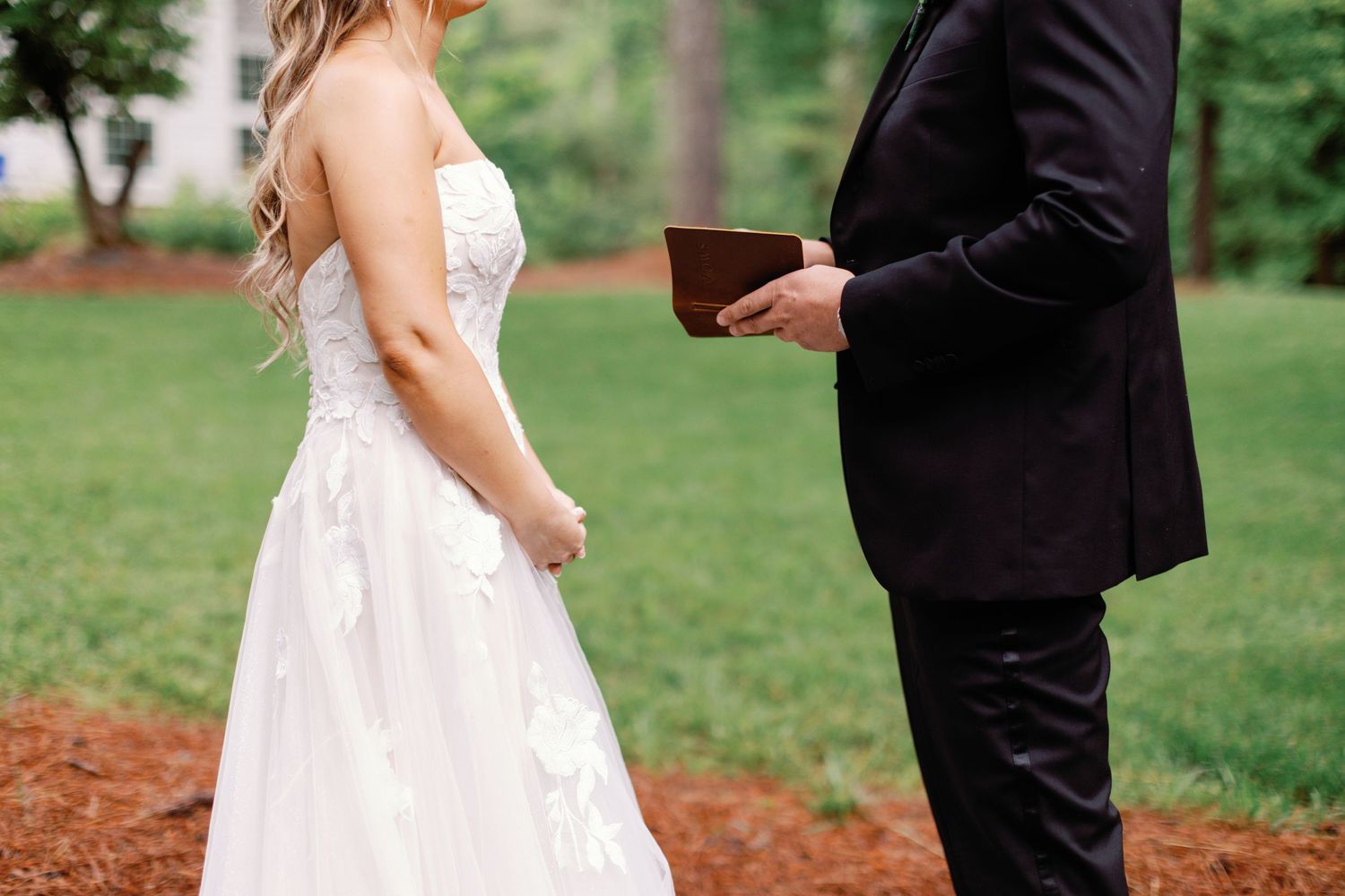 A couple in wedding attire stand together on a garden path during their special day.