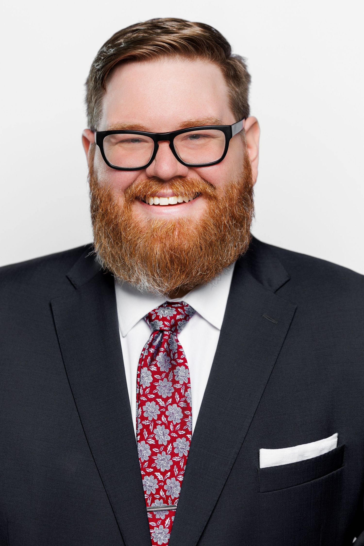 Professional headshot series showing a bearded person in glasses and dark suit with red patterned tie against white background.