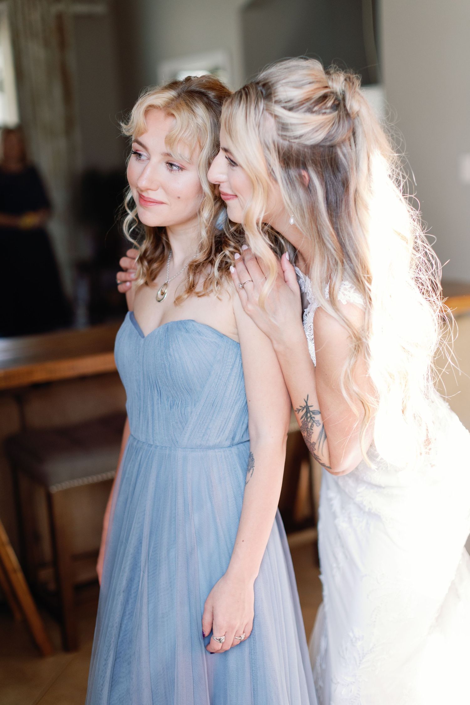 Two women share laughter together, one in a white dress and one in a light blue bridesmaid gown.