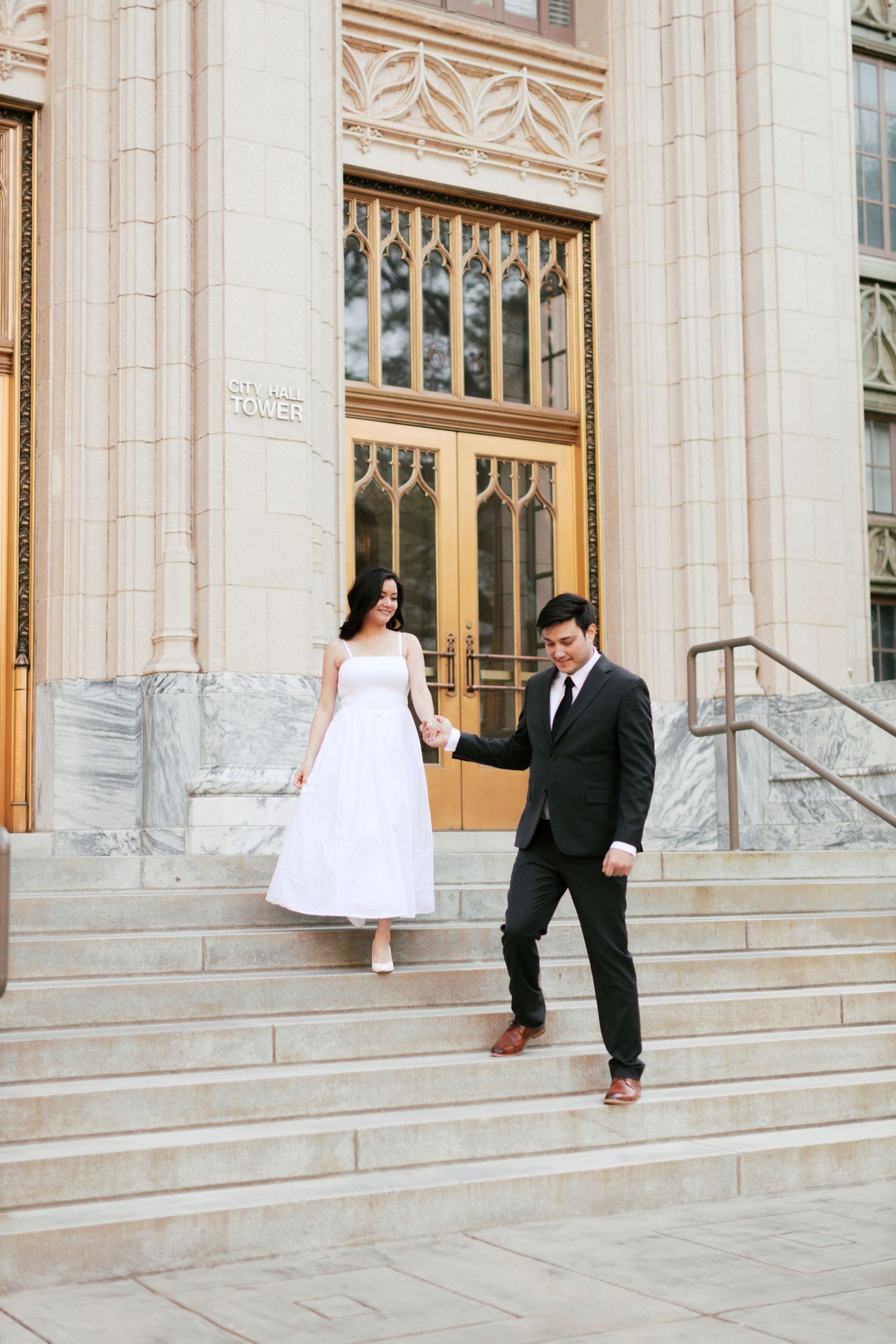 Elegant couple in formal attire posing playfully on grand stone steps of a historic building.