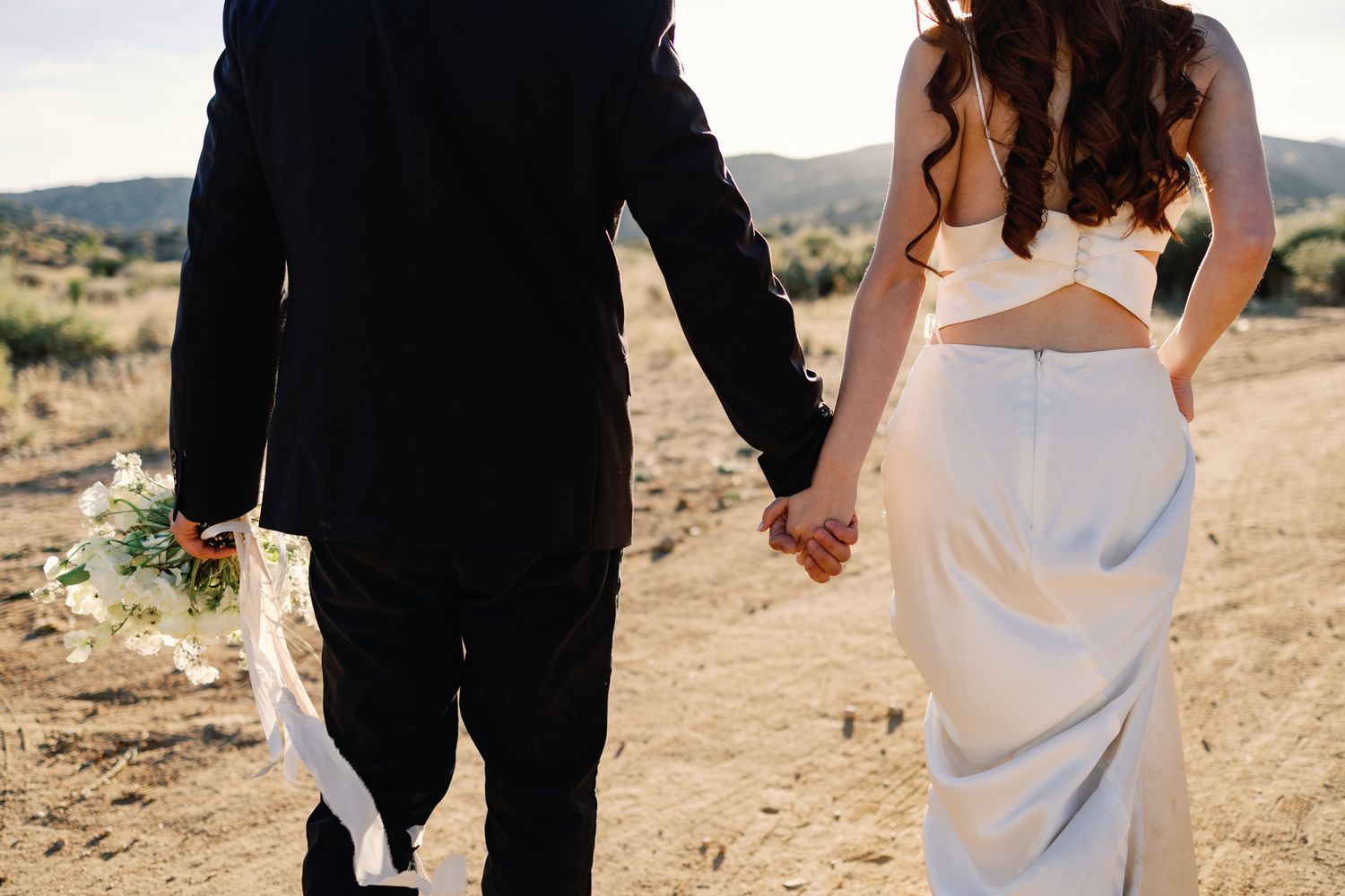 Wedding couple holding hands walking through desert landscape.