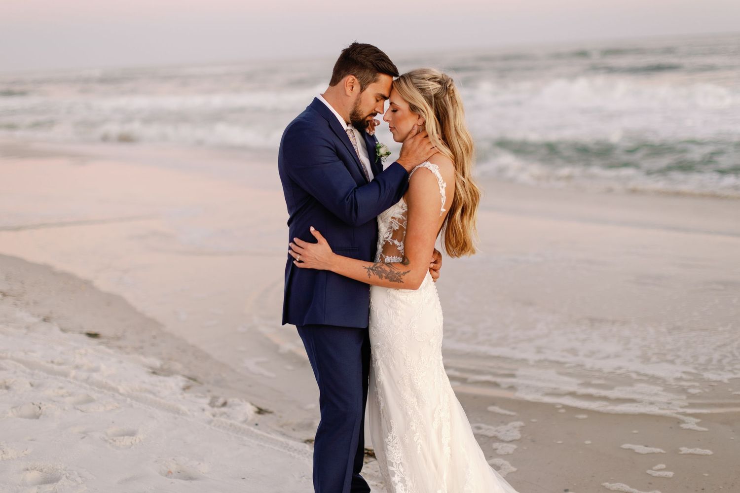 Bride and groom share intimate moments by the ocean during sunset photoshoot.