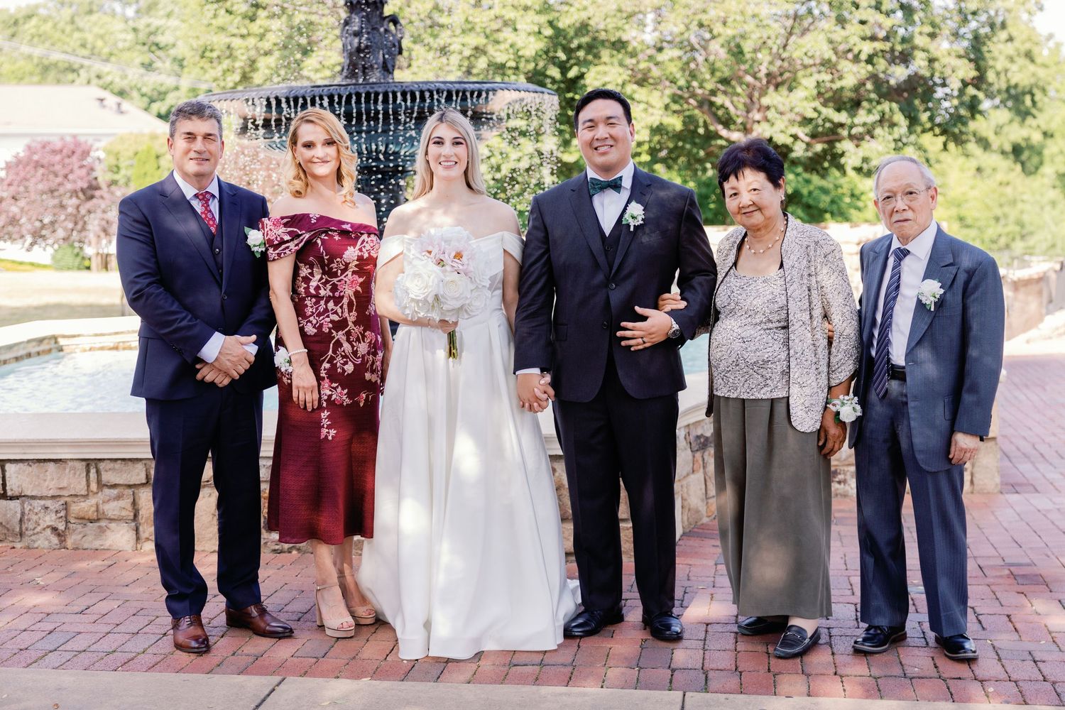 Wedding party poses together on brick walkway with bridesmaids in burgundy dresses.