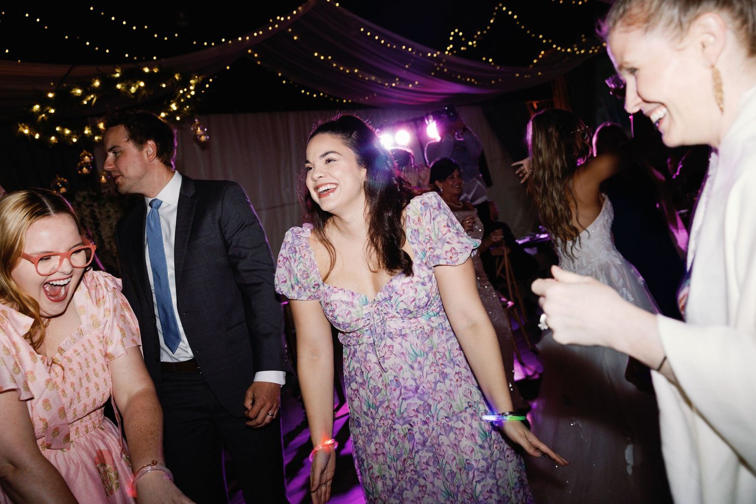 Wedding guests enjoying themselves on a dance floor under decorative lighting.