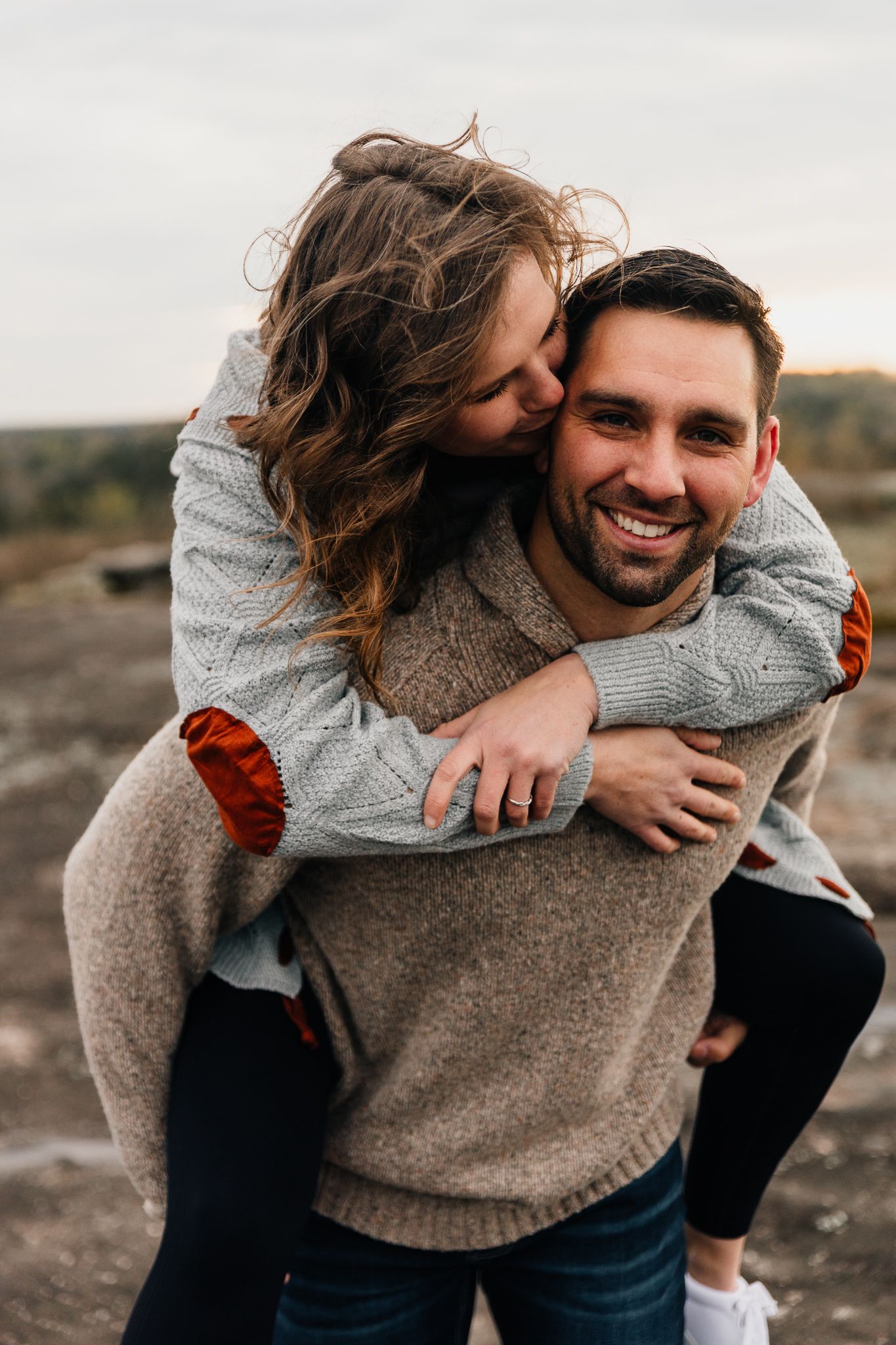 Couple sharing playful piggyback ride moments in cozy sweaters outdoors.