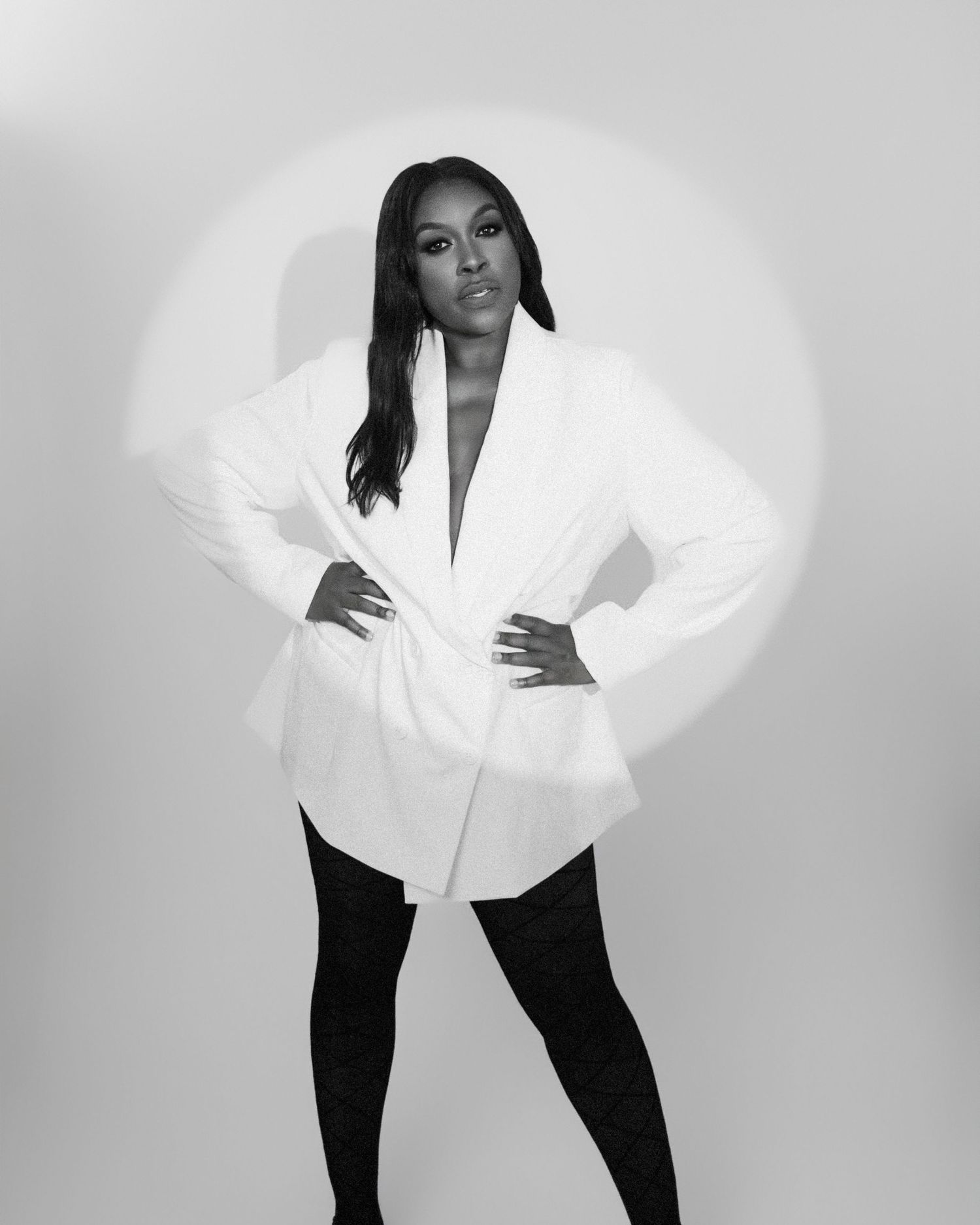 Model strikes dynamic poses in white blazer and black pants during studio photoshoot.