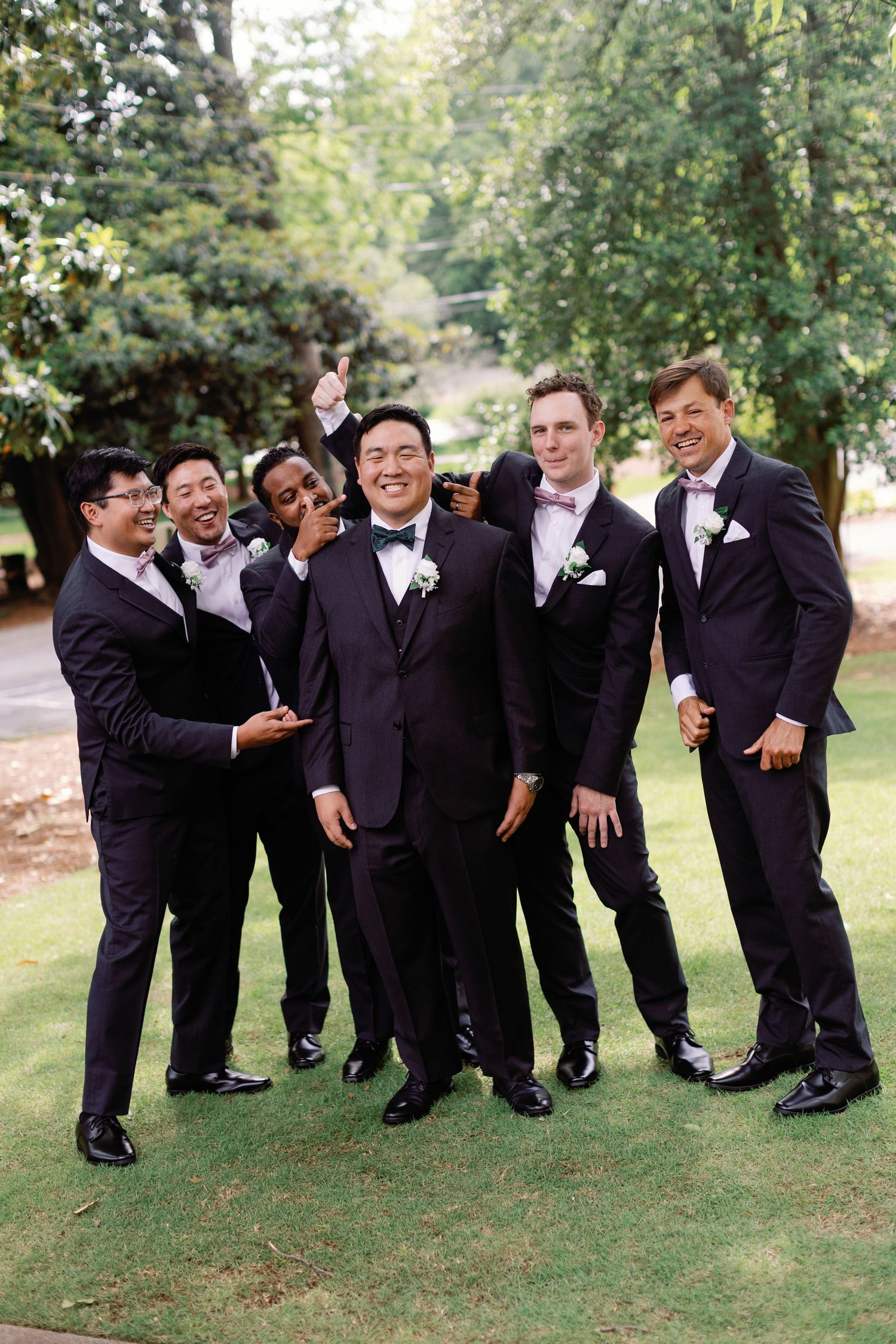 Groomsmen laugh and joke while posing for casual photos on the lawn.