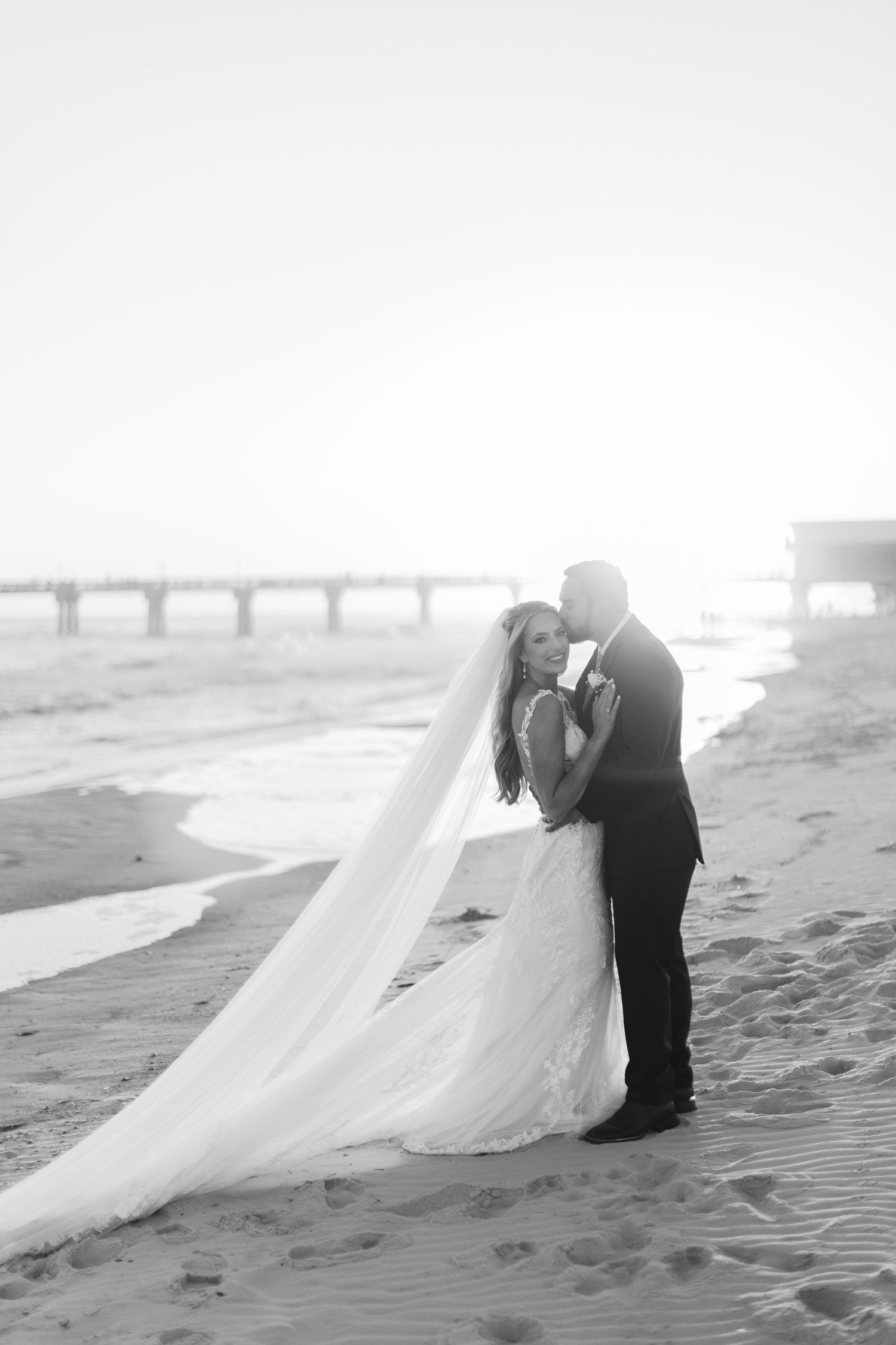 A romantic black and white beach wedding photo sequence with flowing white dress in the sand.