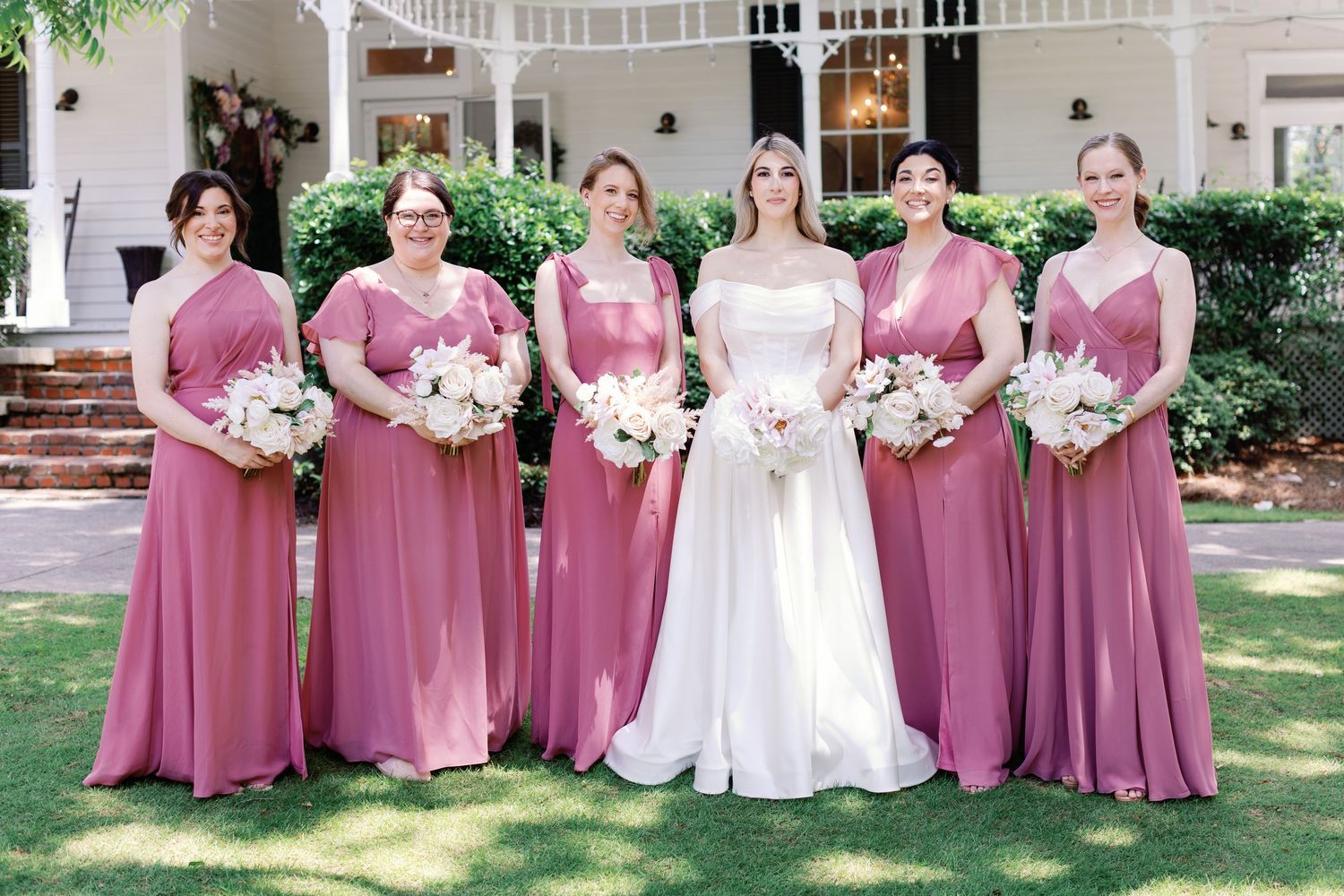 Wedding party in pink bridesmaid dresses and white bridal gown posing outdoors.