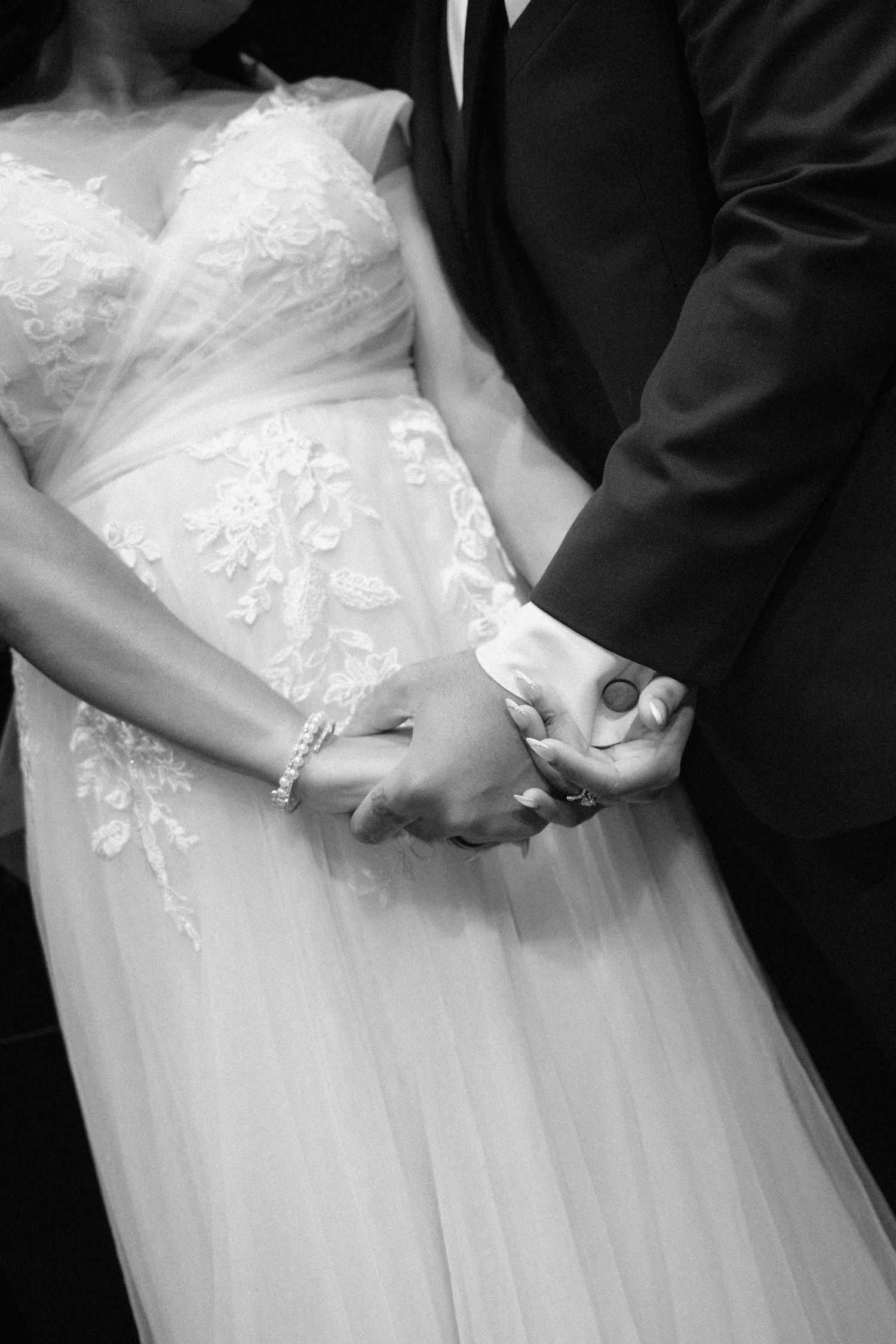 Close-up details of bride's lace wedding dress and hands.