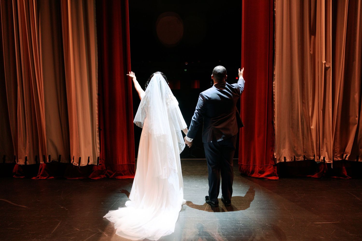 A dramatic silhouette of a couple on stage with red curtains and flowing white wedding dress veil.