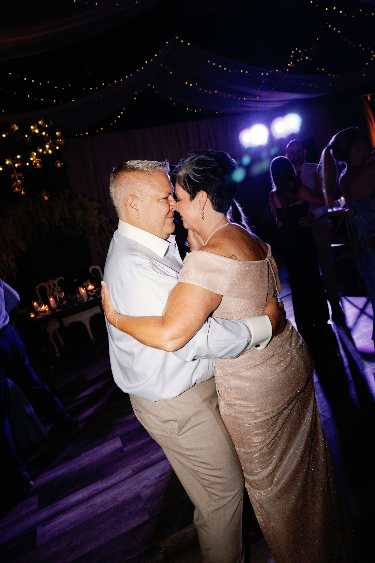 A couple shares an intimate dance moment under purple lighting at their wedding reception.
