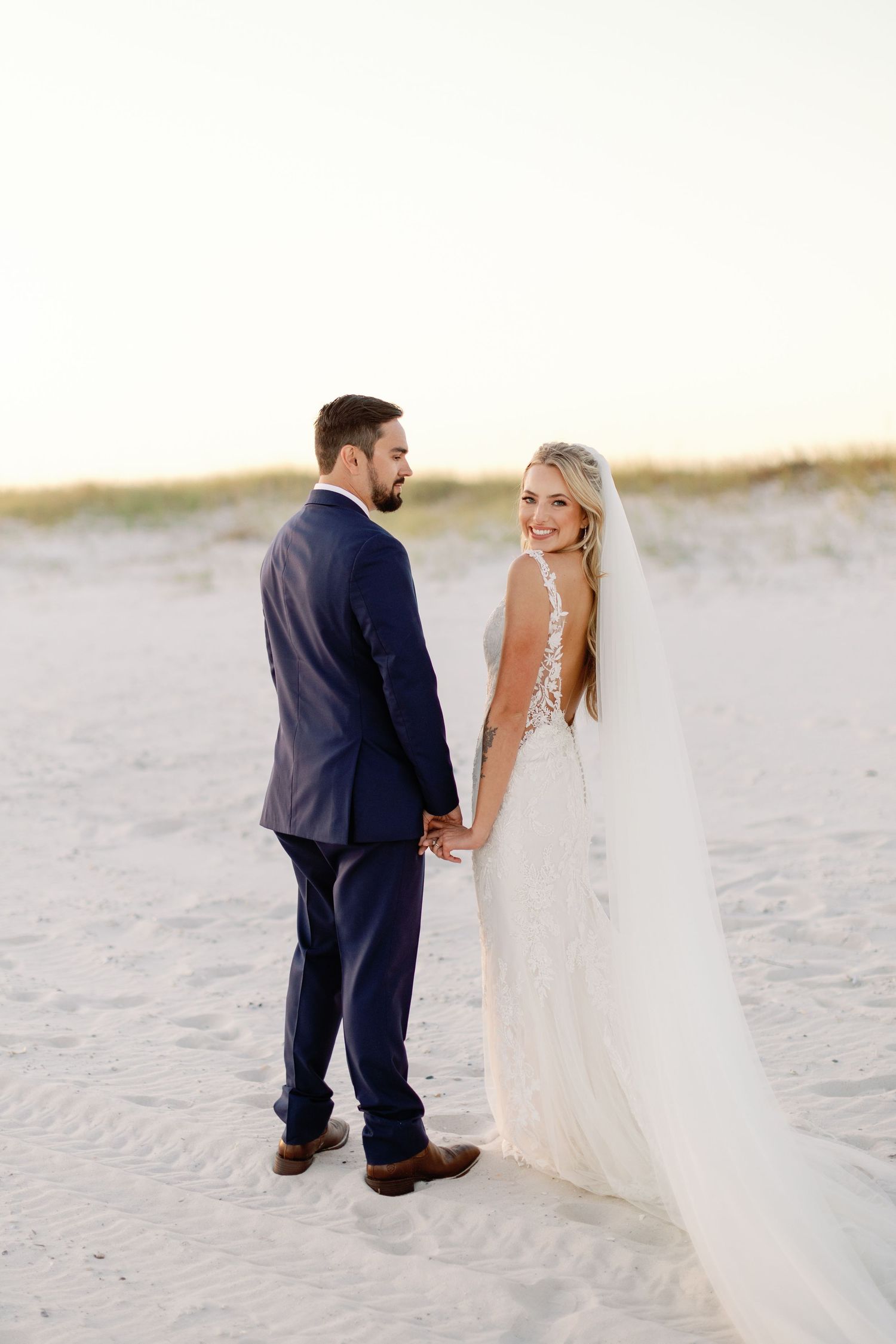 A romantic beach wedding photo series showing a couple walking in the sand at sunset.
