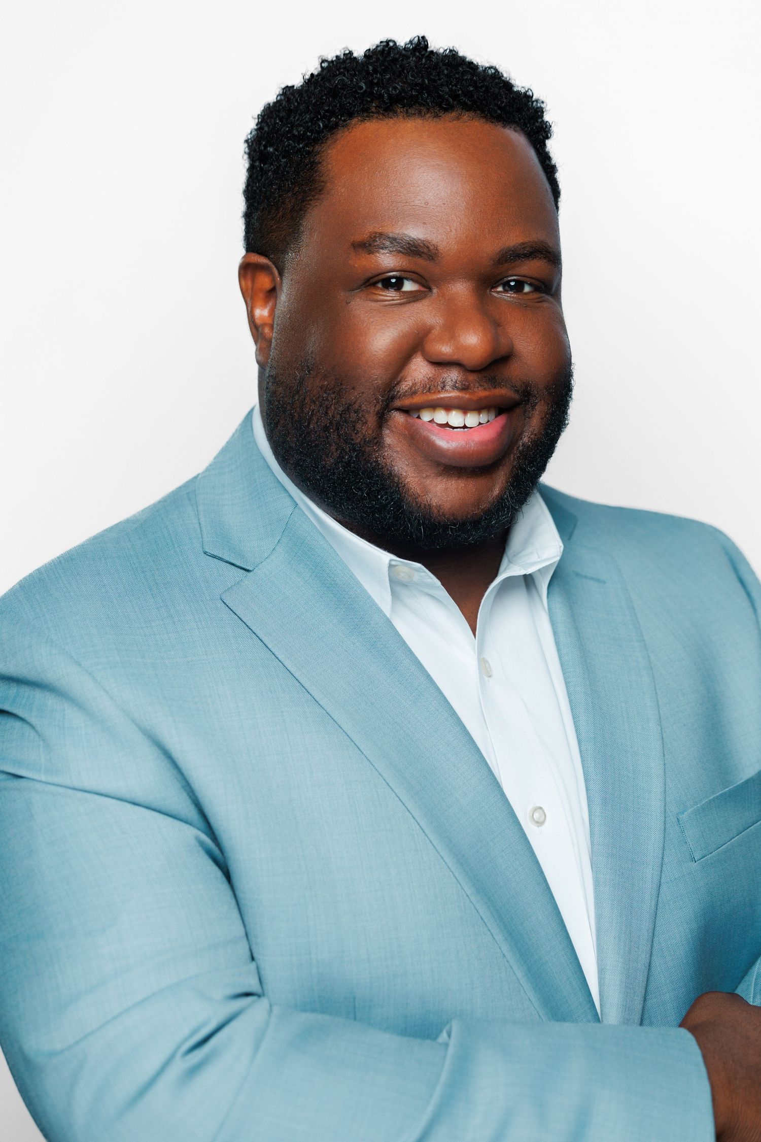 Professional headshot of someone wearing a light blue blazer and white shirt against a white background, smiling warmly.