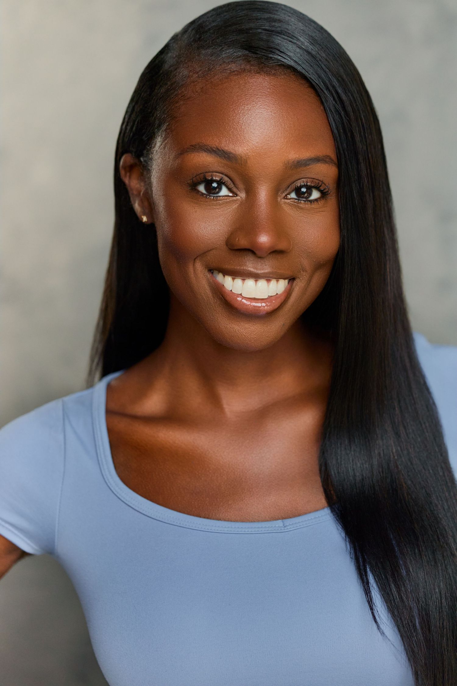 Smiling young Black woman with long straight hair wearing a light blue top in a professional headshot photo.