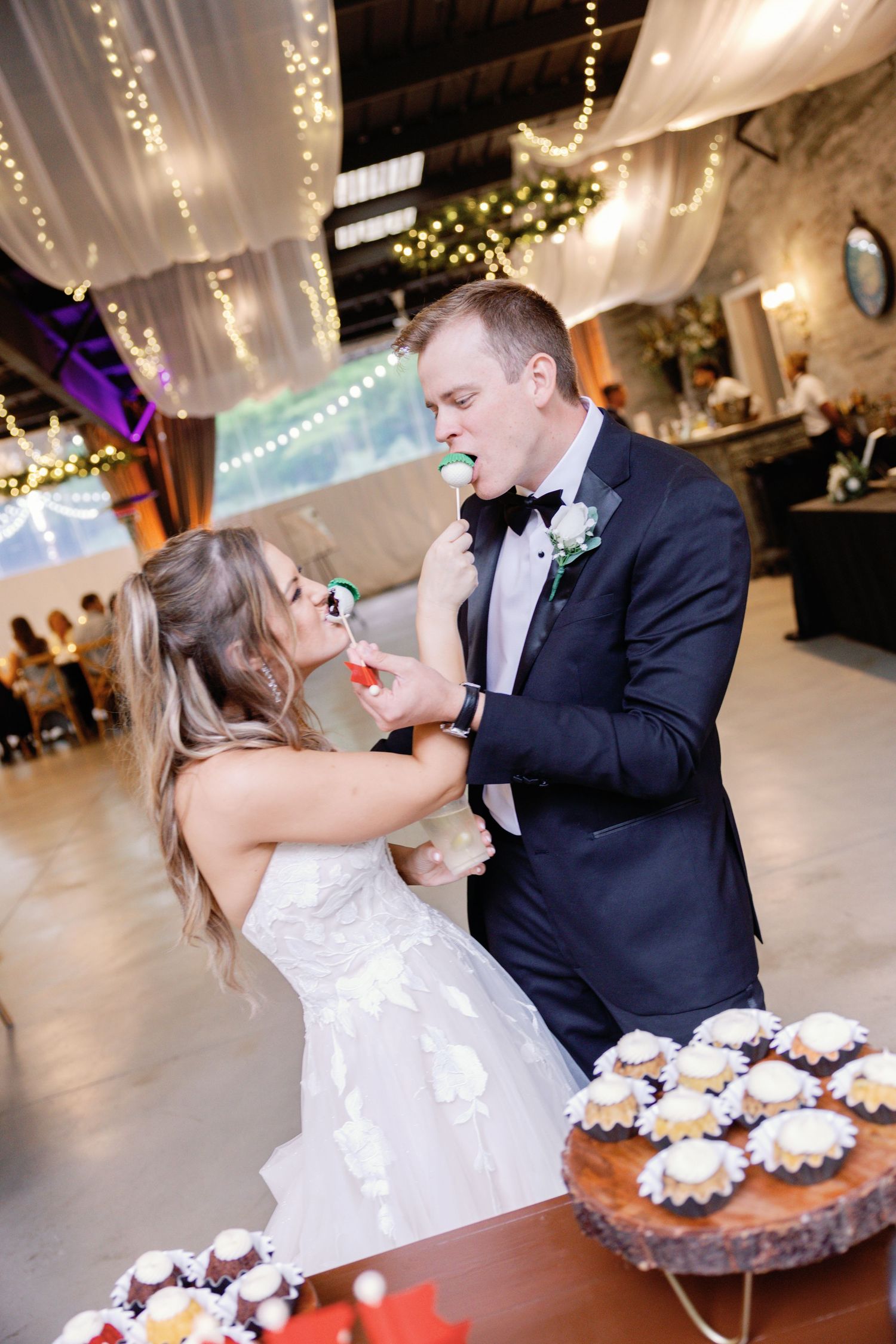 Couple shares playful cake-cutting moment during wedding reception in decorated indoor venue.