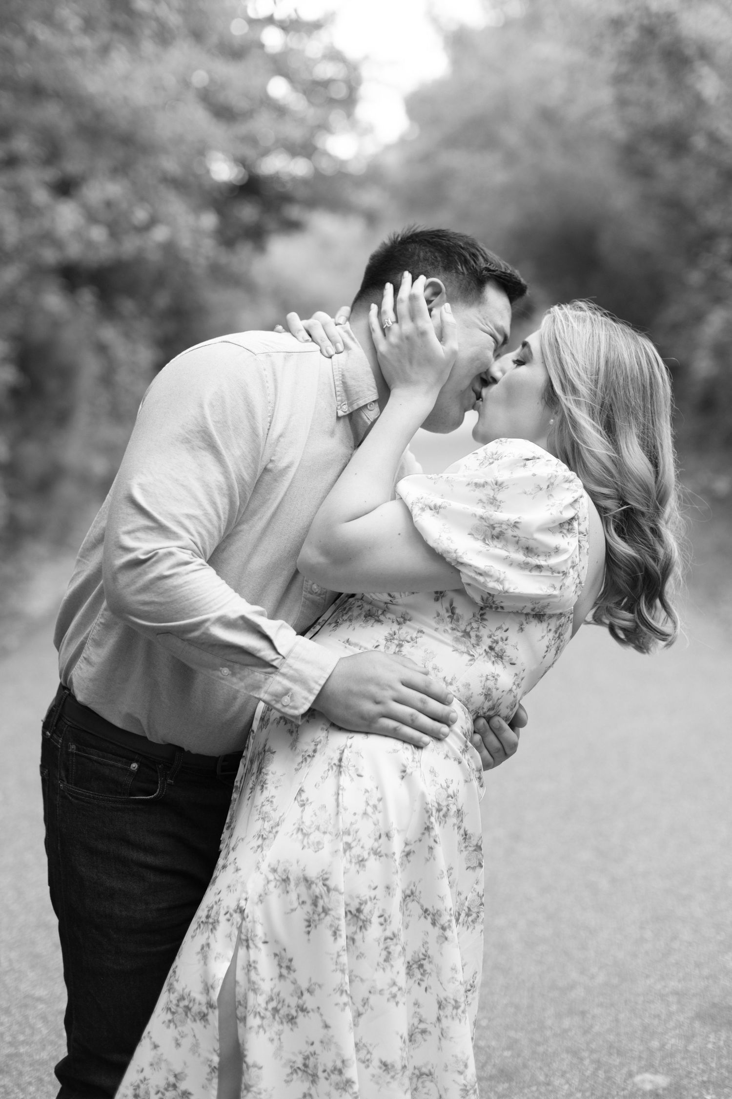 Romantic couple embracing in a garden setting with soft natural light filtering through trees.