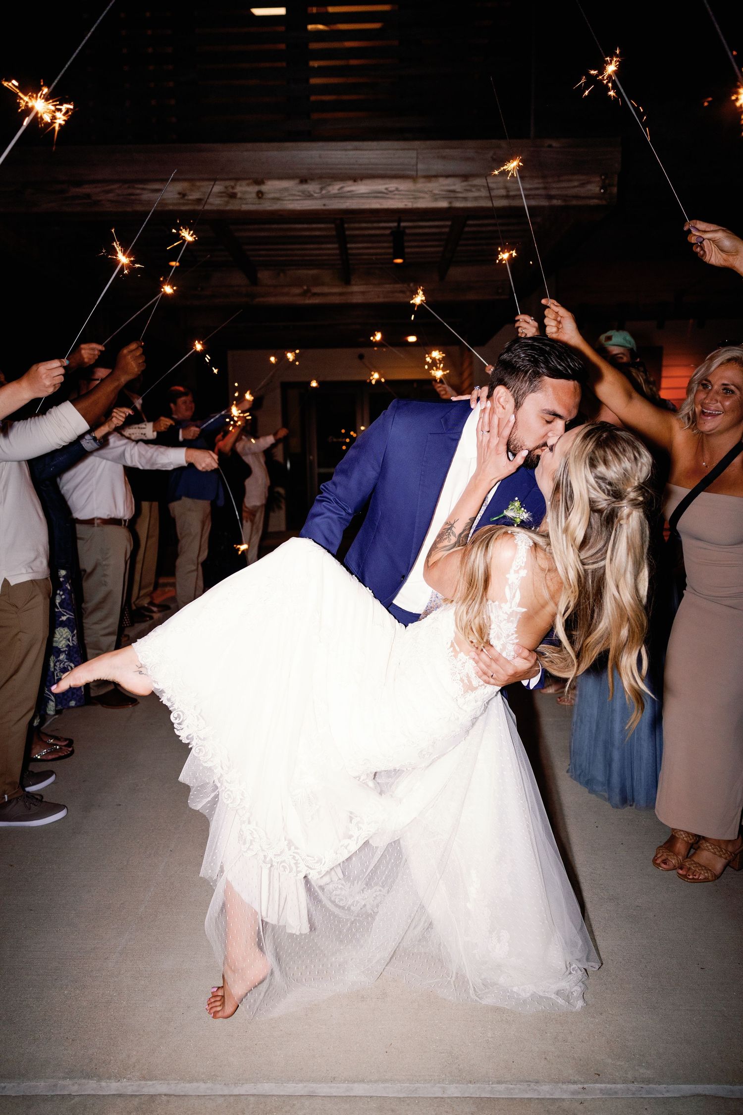 Couple and guests dancing with sparklers in a rustic indoor venue.