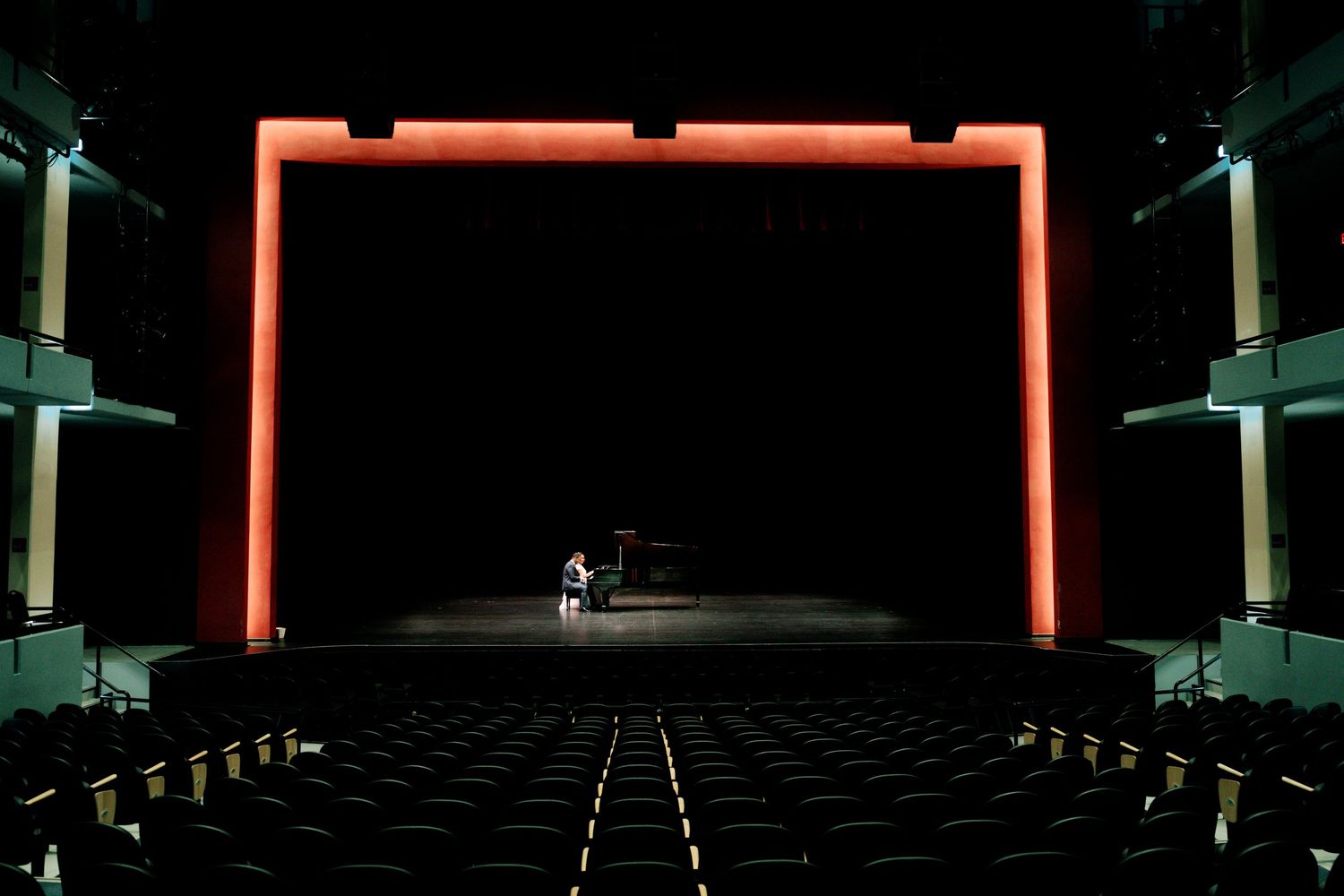 Dark empty theater stage with red lighting elements and architectural details.