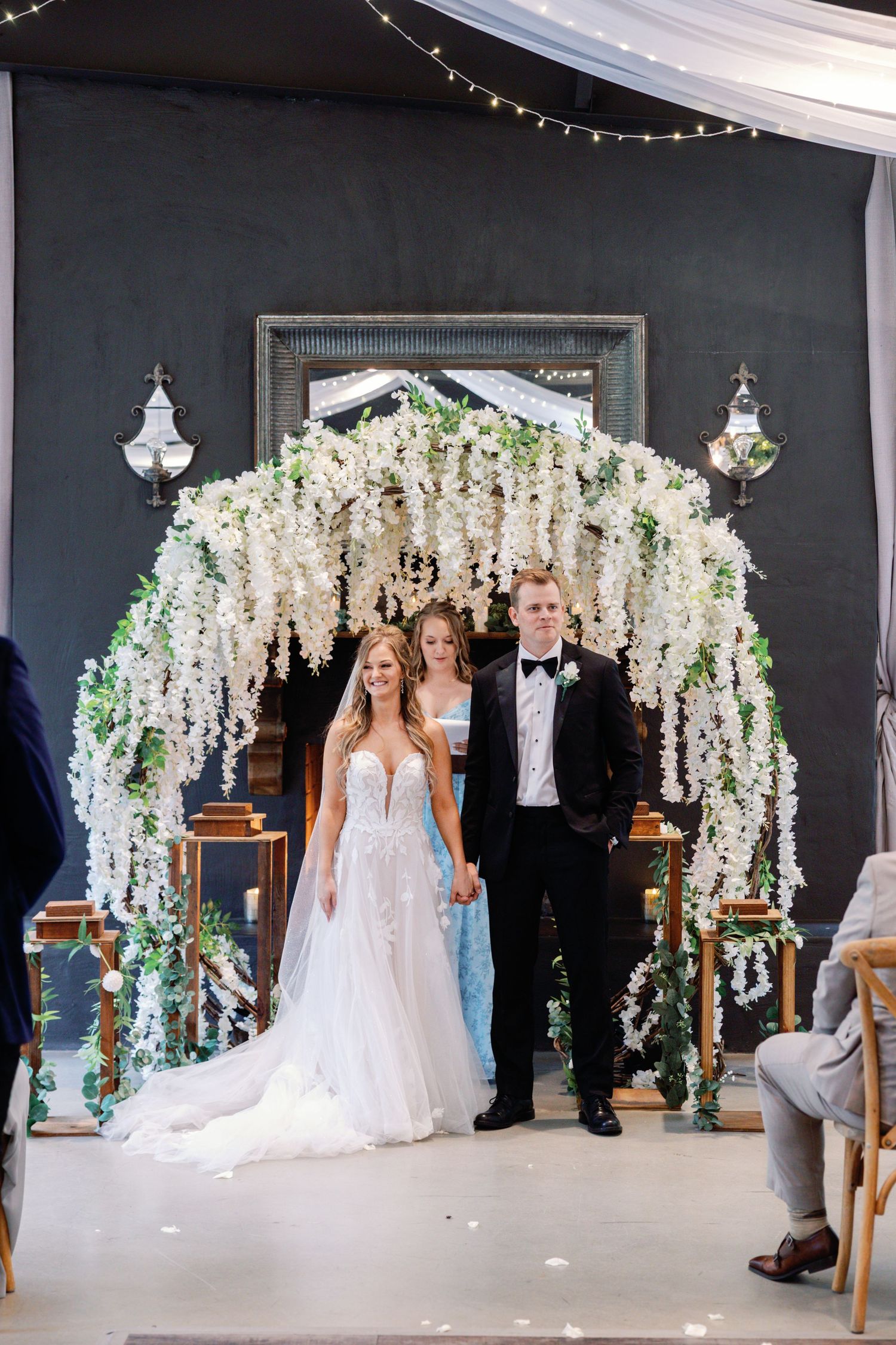 An elegant wedding ceremony setup with cascading white wisteria floral arches against a dark backdrop.