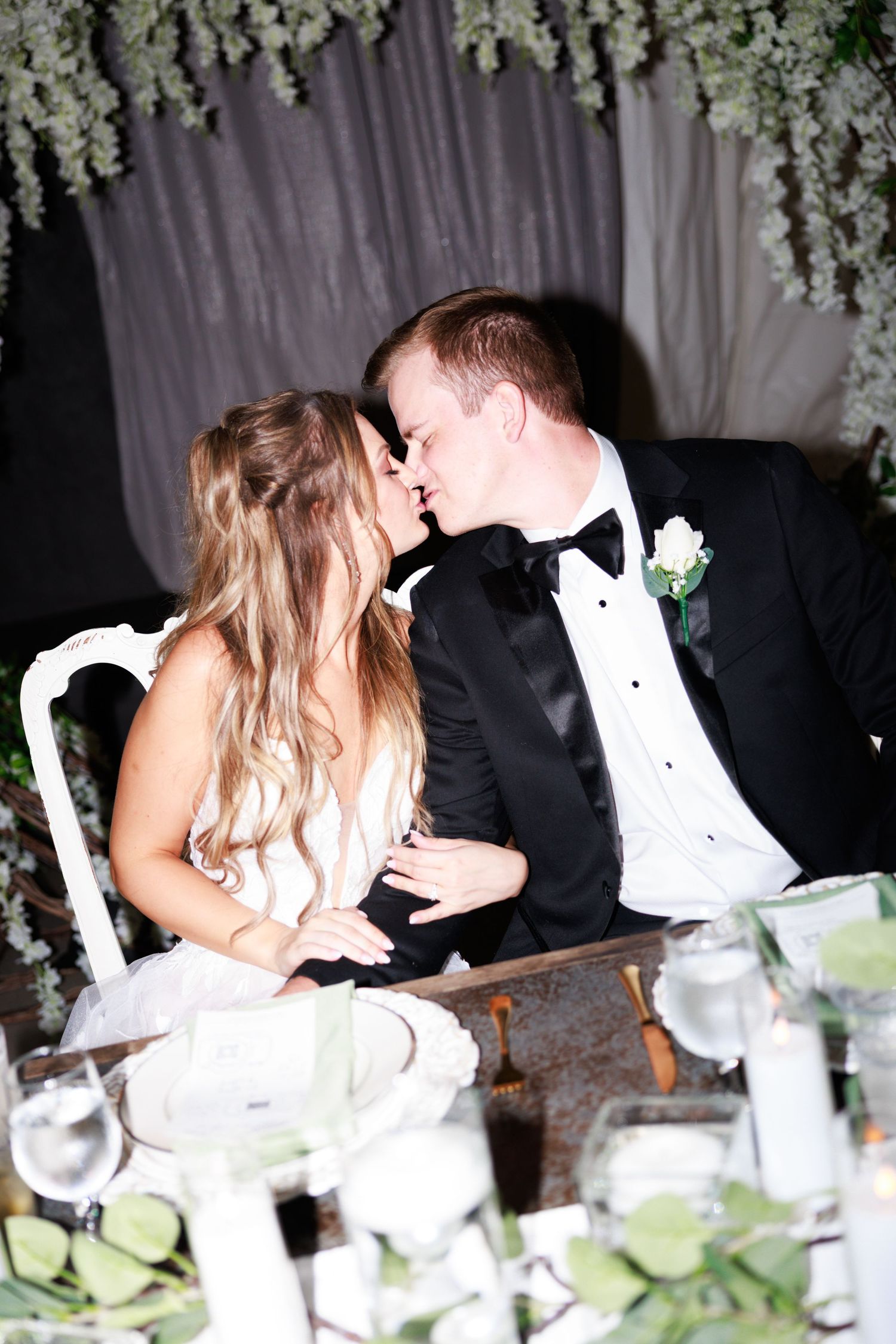Romantic moment captured at wedding reception with floral decor and white drapery.