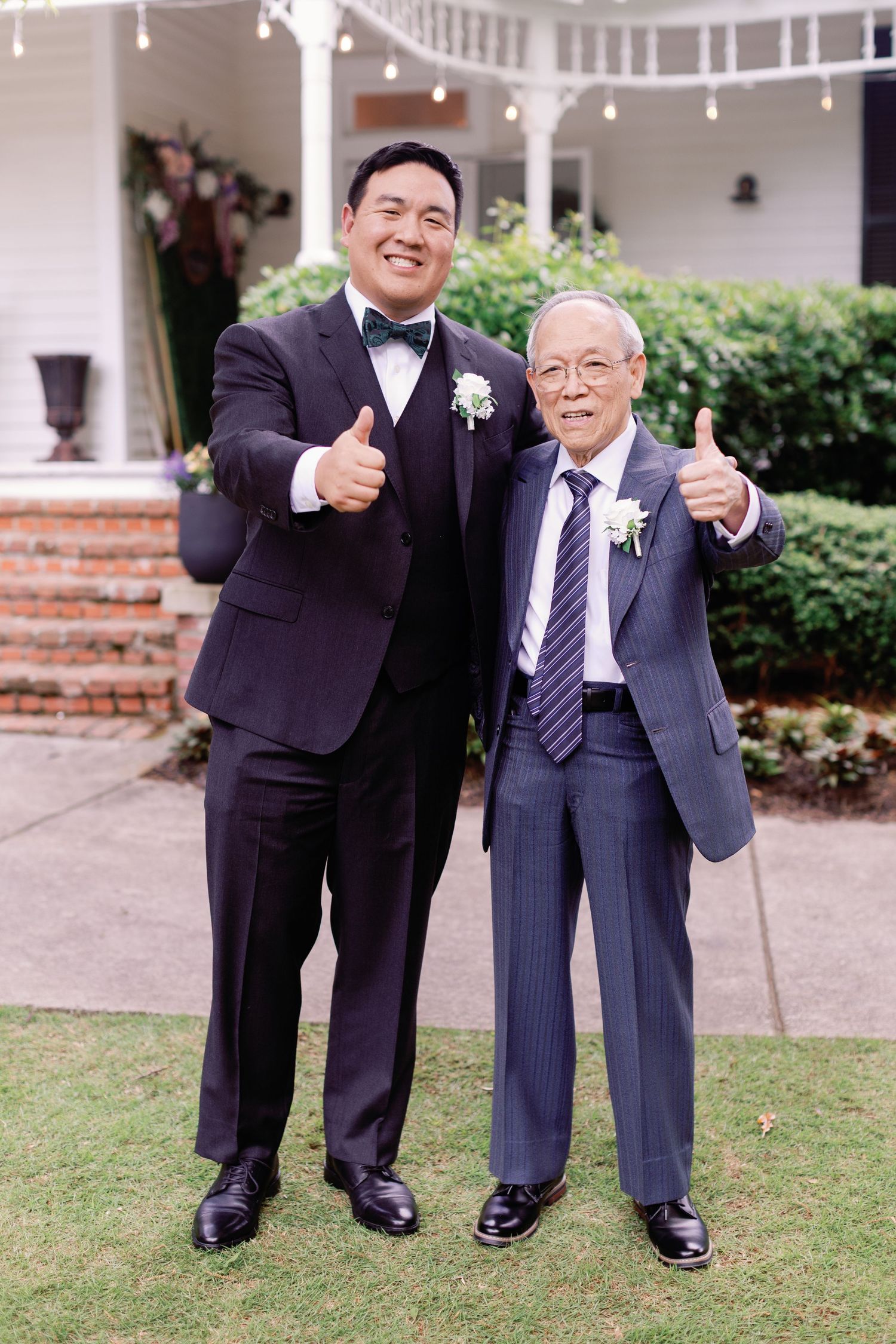 Joyful wedding family portraits with men in dark suits on garden grounds.