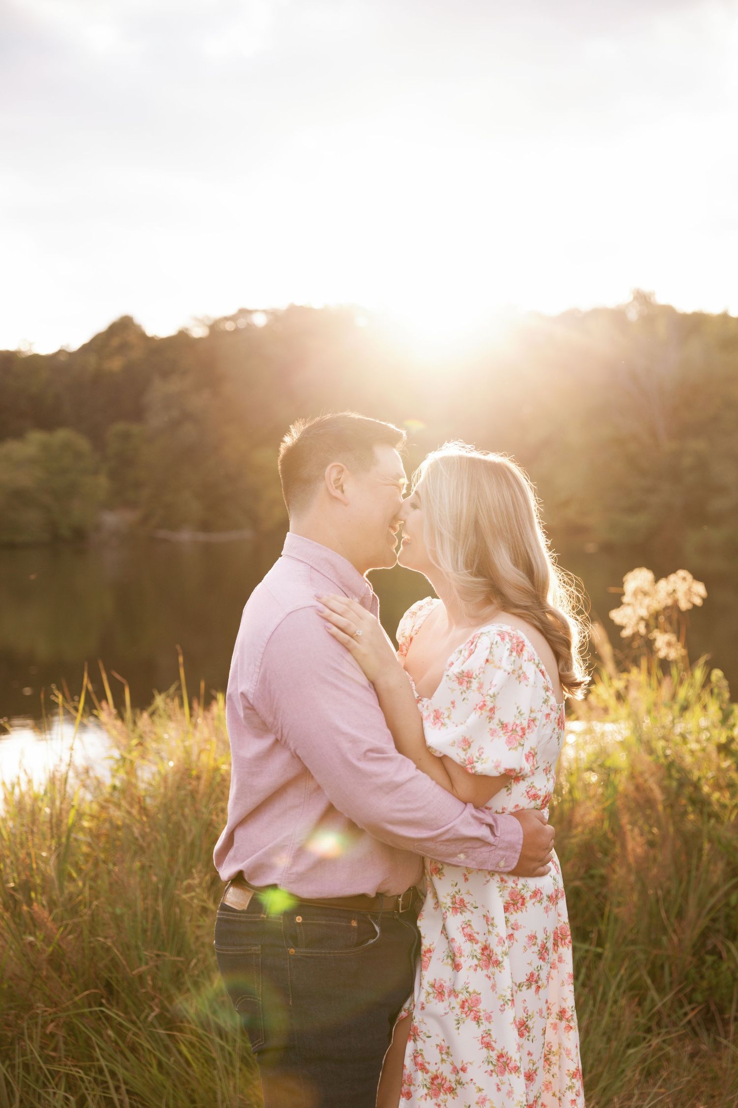 Couple sharing an intimate moment in a field during golden hour with sunlight creating a dreamy atmosphere.