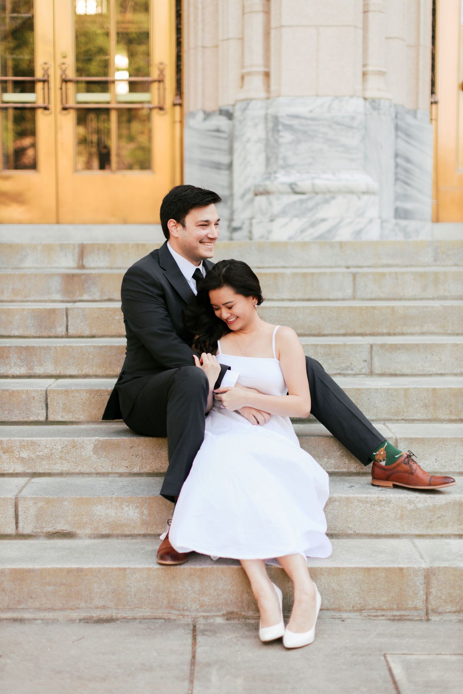 Couple sitting playfully on marble steps in formal attire.