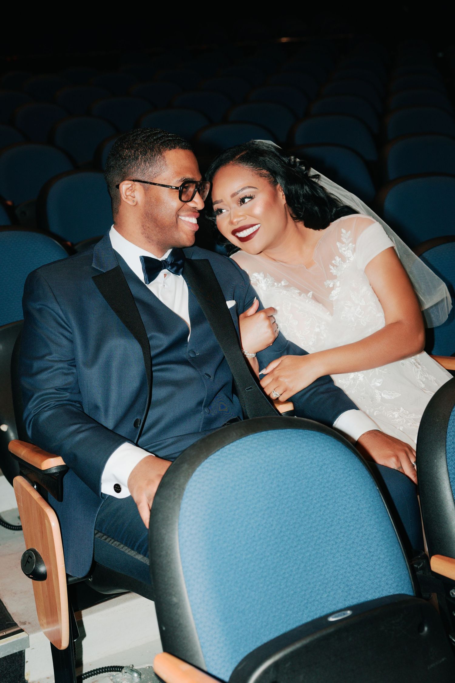 Couple in wedding attire sharing intimate moments in blue theater seats.