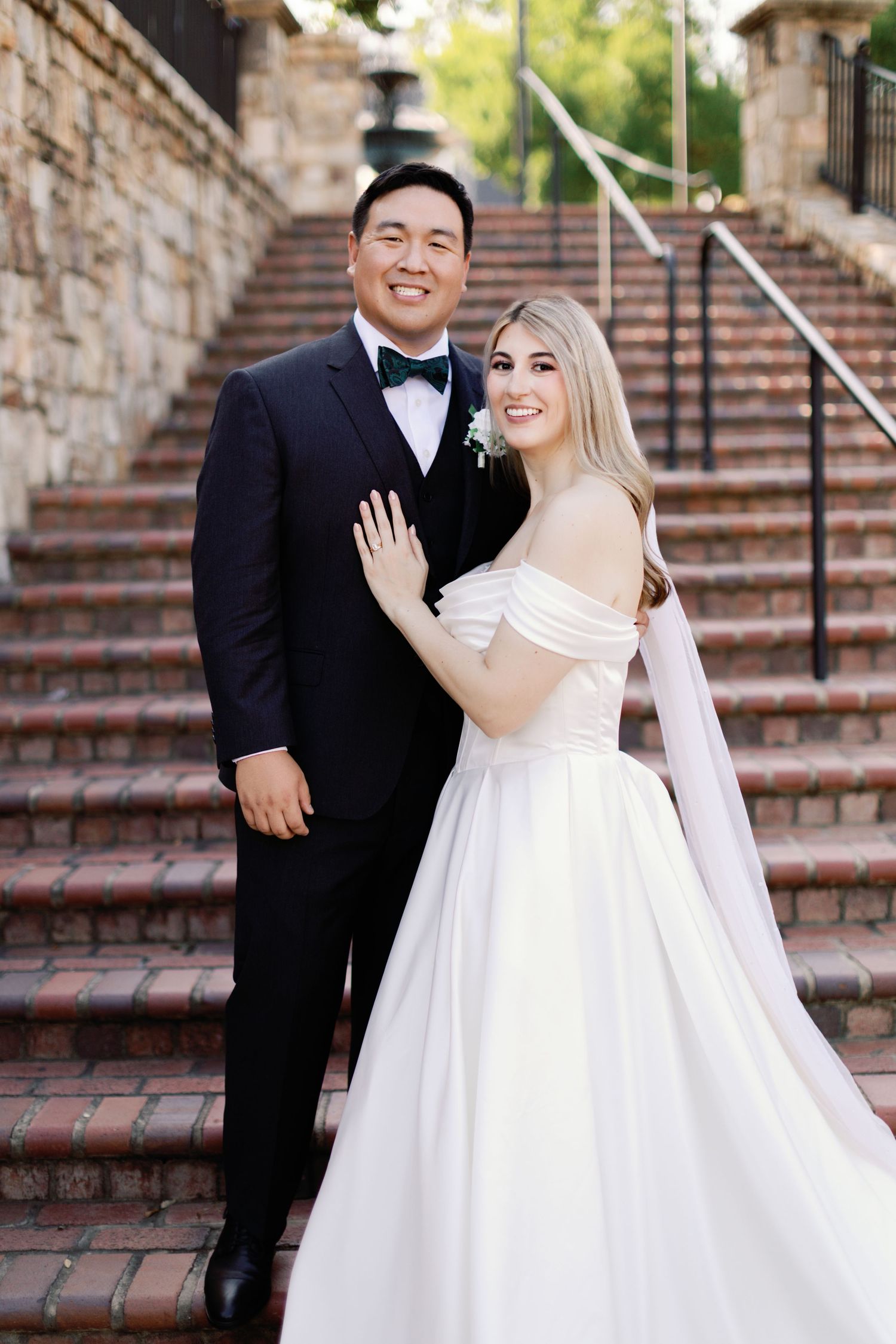Wedding couple poses on elegant stone staircase in formal attire.